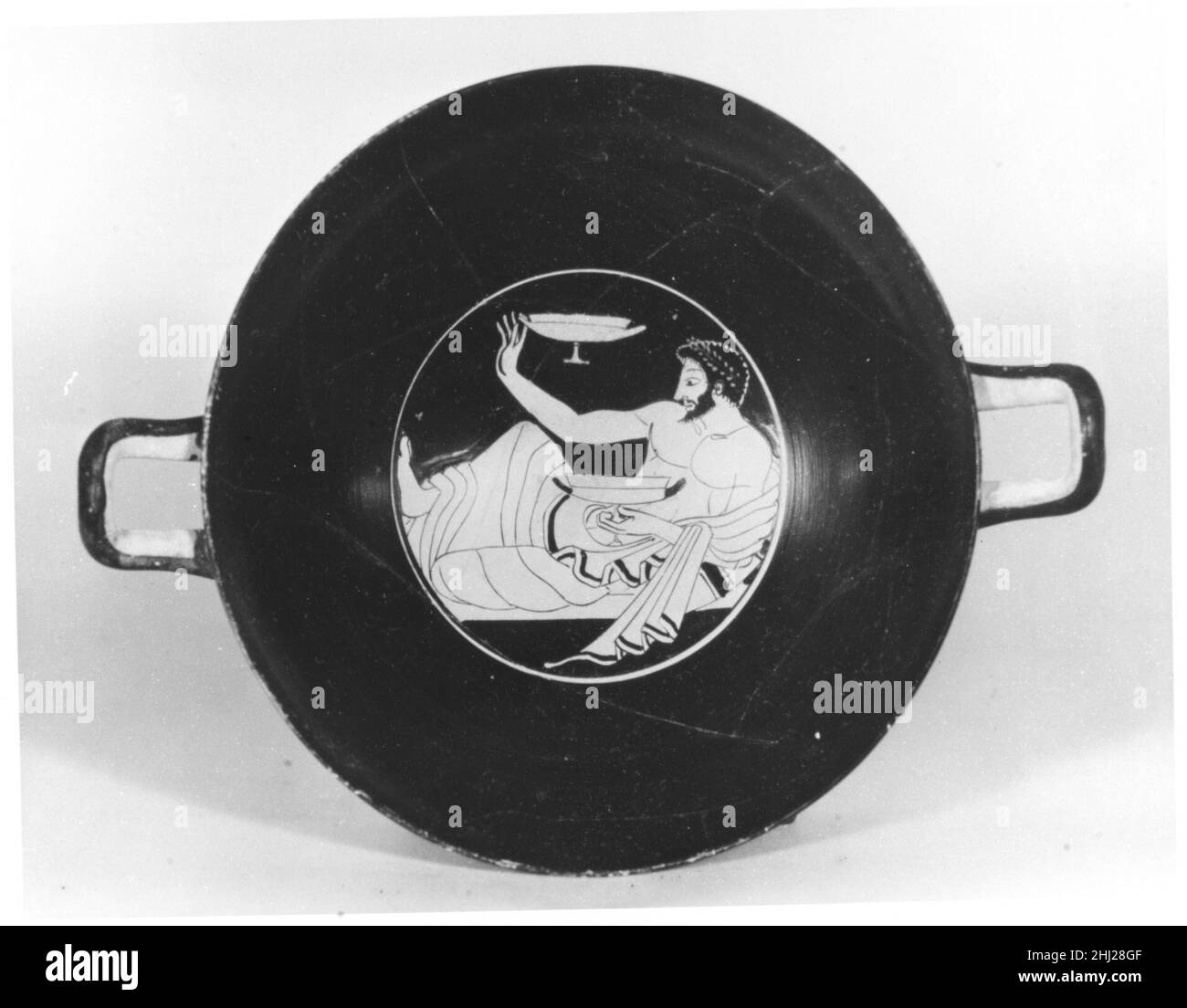 Kylix di terracotta ca. 500 a.C. attribuito ad un artista vicino al Kleophrades Painter Interior, simposista (partecipante al party) noto principalmente per il suo lavoro su pentole, il Kleophrades Painter è anche associato a kylike sia all'inizio che alla fine della sua carriera. L'uomo qui raffigurato tiene una tazza, presumibilmente piena di vino, nella sua mano sinistra. Con la tazza nella mano destra gioca kottabos, un passatempo dopo cena in cui i simposi hanno bussato le finali fuori dalla lampada, con i lees rimasti nei loro kylike. Chilix di terracotta (tazza da bere) 254921 Foto Stock