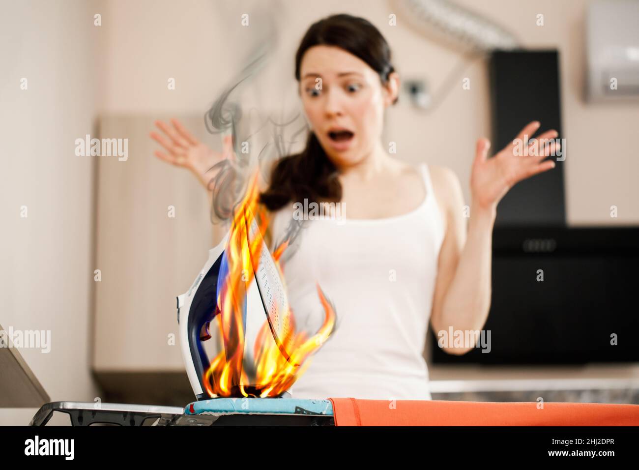 Una donna urla nel panico quando vede un ferro che brucia. Cause di accensione e incendio nell'alloggiamento. Sicurezza antincendio e antincendio. Foto Stock