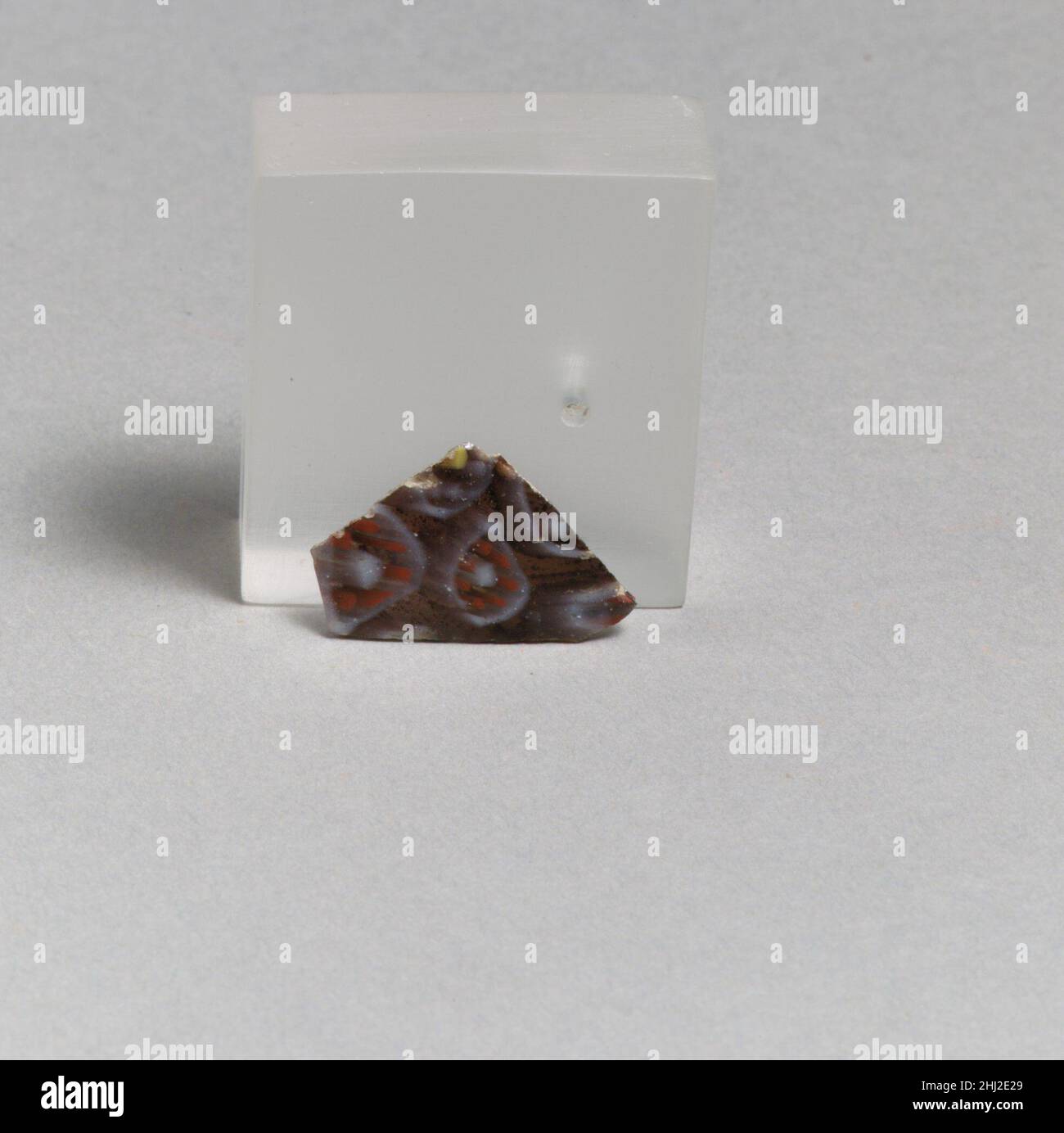 Frammento di mosaico di vetro fine 1st secolo a.C.–inizio 1st secolo d.C. romano frammento di corpo a pareti sottili.viola traslucido, bianco opaco, giallo e rosso.lato curvo leggermente convesso; due bordi quasi diritti ad angolo retto rispetto a ogni other.Composite motivo di mosaico formato da sezioni poligonali di due canne, entrambi in un terreno viola: Uno con un cerchio bianco intorno ad un anello di aste rosse e un'asta centrale bianca, e l'altro con un cerchio bianco intorno ad un anello di aste bianche e un'asta centrale gialla.uno spigolo rotto e intemperato; esterno lucido; vaiolatura e intemperatura di bolle di superficie su exteri Foto Stock