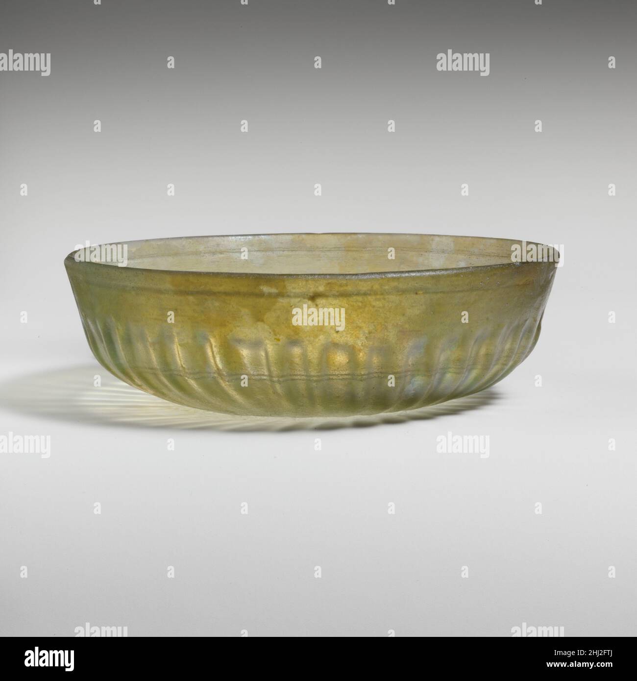 Vetro costato ciotola fine 1st secolo a.C.–metà 1st secolo d.C. romano traslucido giallo chiaro verde.semplice ma leggermente irregolare, bordo arrotondato; Lati rastremati verso il basso, quindi incurvati verso il basso leggermente spinti e disomogenei. Sulle scanalature interne orizzontali tagliate a ruota, comprendenti una scanalatura singola più ampia al di sotto del cerchione ed una fascia di due scanalature più strette attorno al corpo inferiore; All'esterno, trentasei costole, distanziate irregolarmente e di diversa lunghezza e spessore, rastremantesi verso il basso, quasi toccando al centro.intatto; bolle di pinprick; dulling, vaiolatura leggera, e iridescente Weathering.greenish poco profondo cast gla Foto Stock
