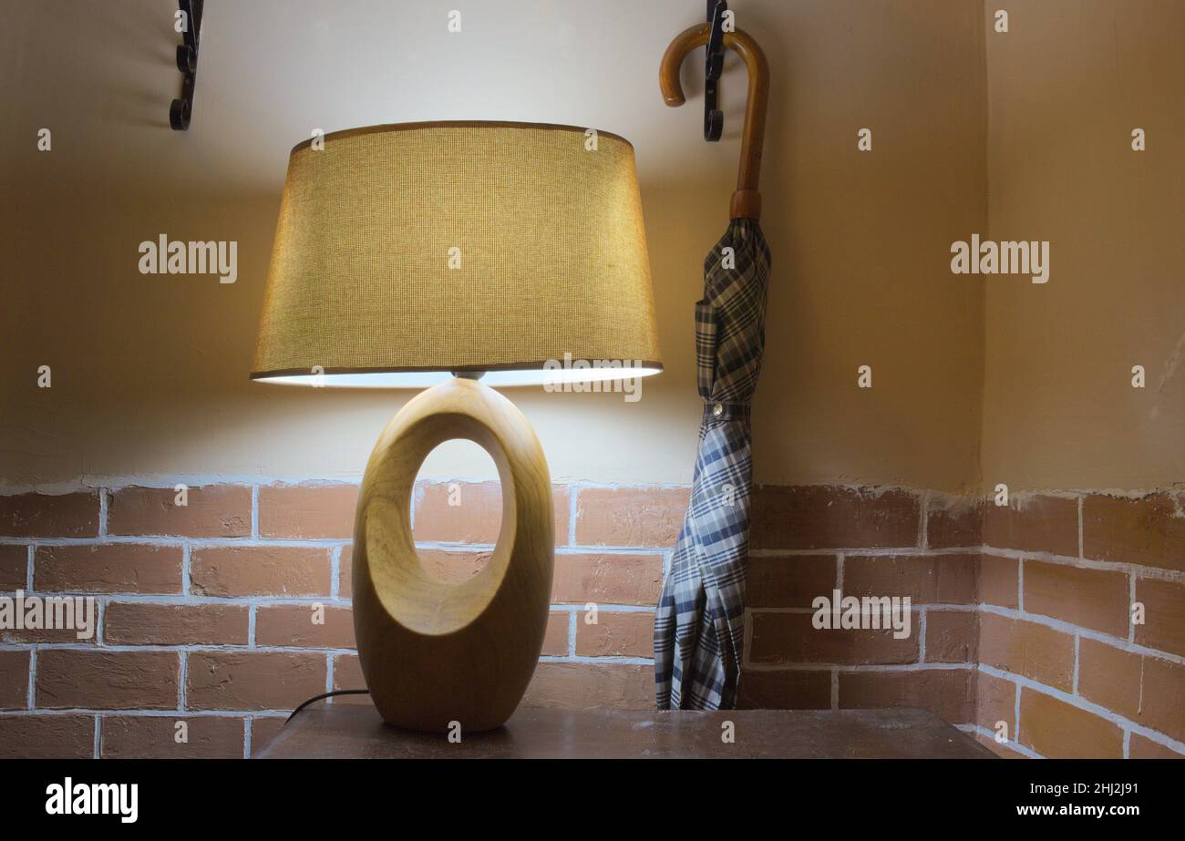 La lampada illumina la parete con mattoni decorativi. Vicino alla lampada è appeso un ombrello. Foto Stock
