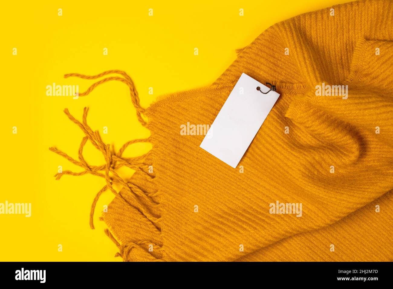 Bella sciarpa gialla calda inverno con etichetta tag mockup modello su sfondo giallo con spazio per il testo, vista dall'alto. Stagione autunnale o autunnale. Foto Stock