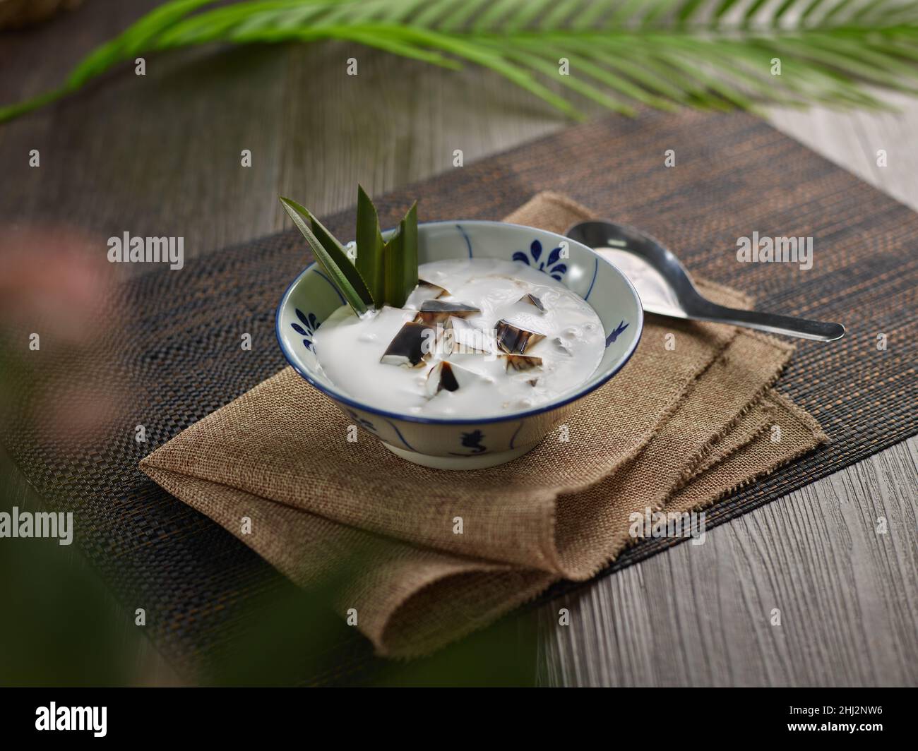Gelatina di erba verde ghiacciata locale indonesiana con latte di cocco in ciotola su tavola di legno Foto Stock