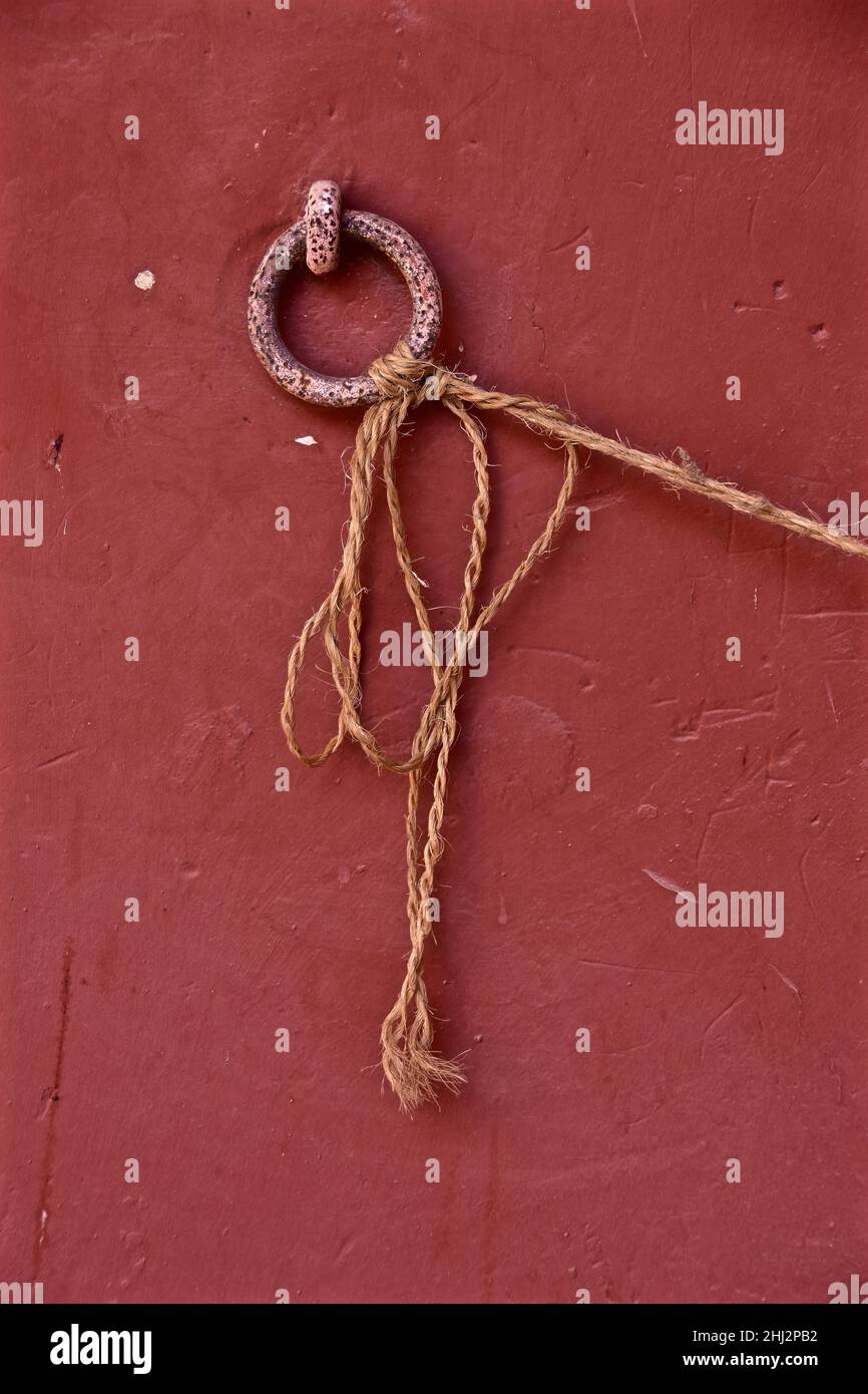 Anello metallico su muro rosso con cavo lungo legato, Spagna Foto Stock