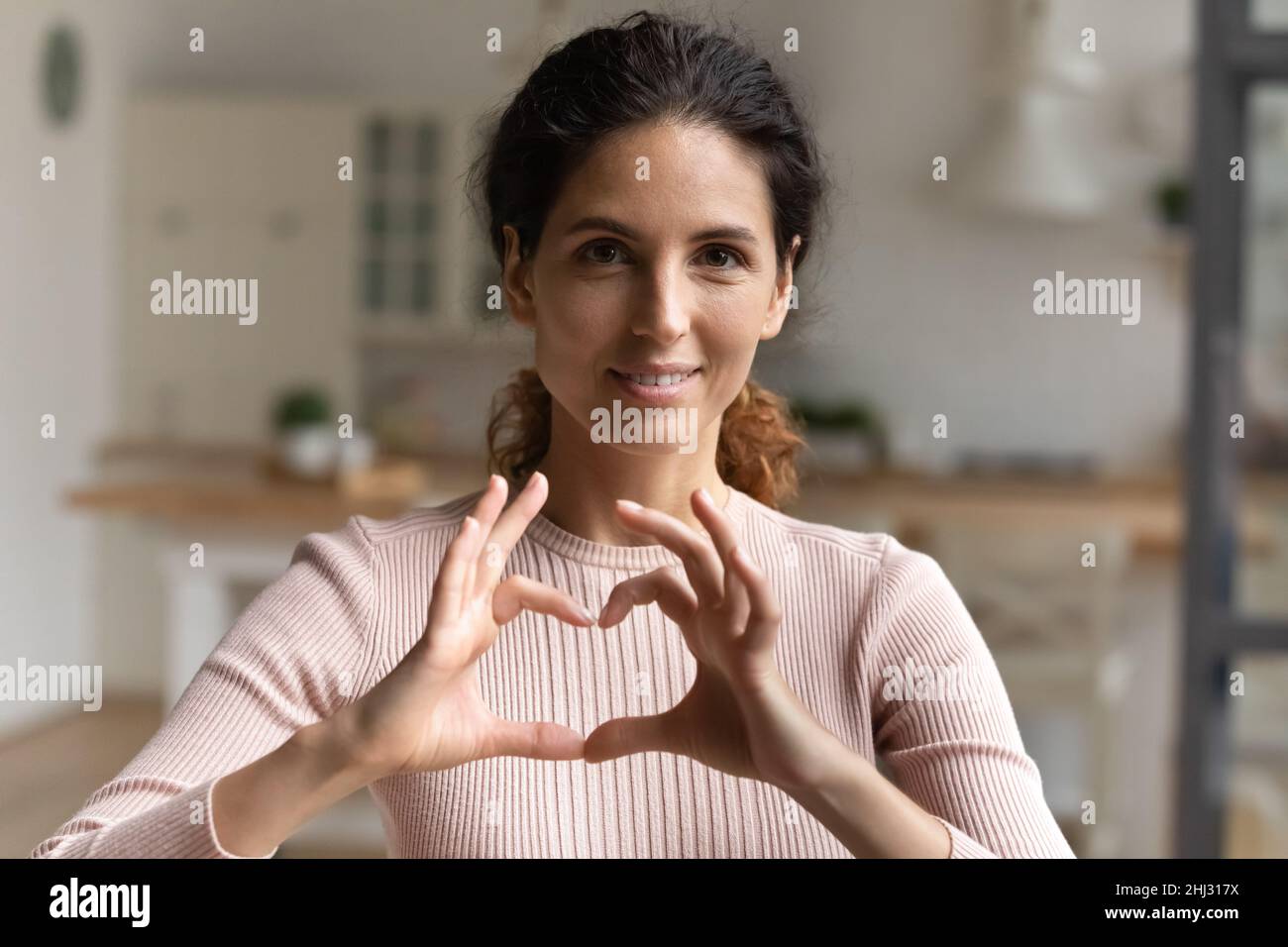 La donna latina fa un gesto di simbolo del cuore con le dita unite Foto Stock