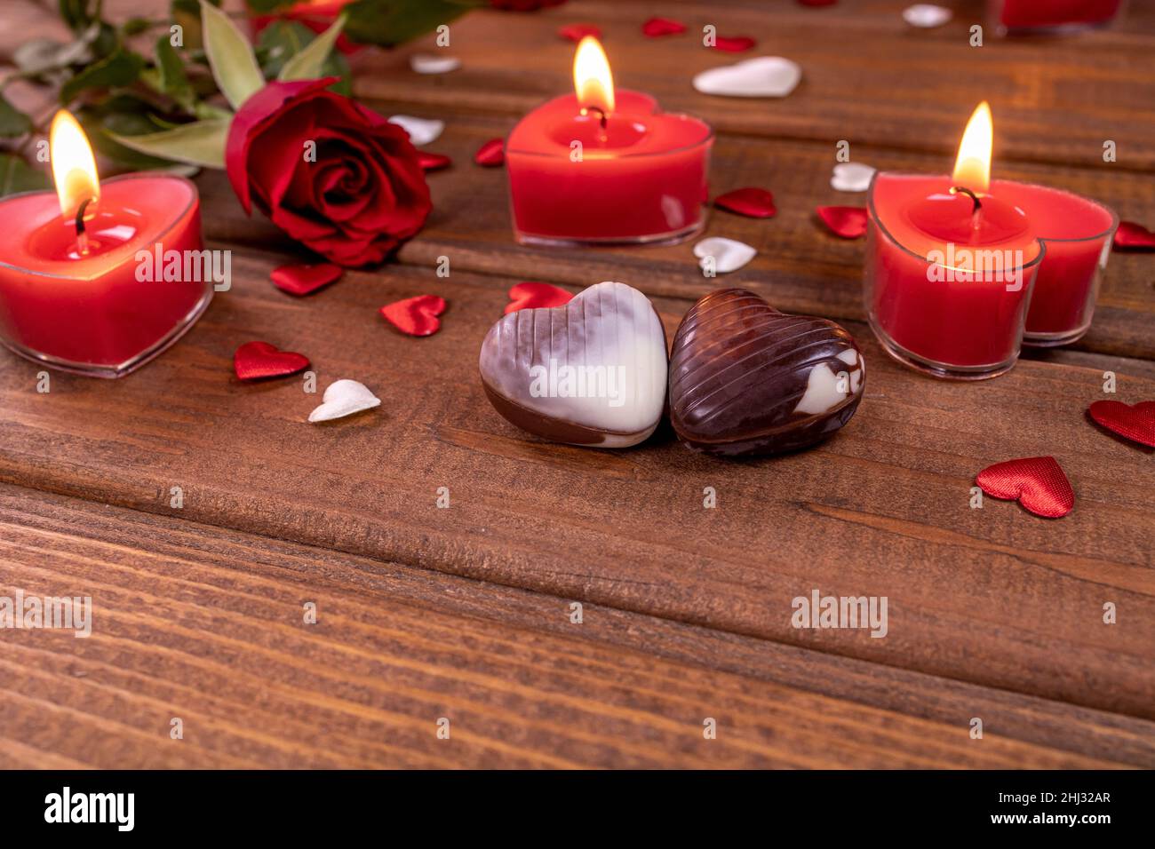 San Valentino concetto cioccolato caramelle a forma di cuore e rose rosse con candele su legno. Concetto di amore e romanticismo. Foto Stock