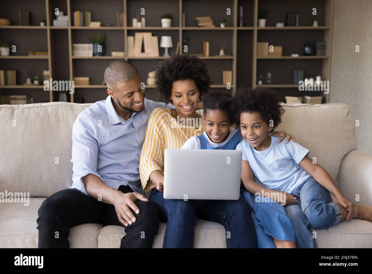 La coppia africana e i bambini si siedono sul divano con un computer portatile Foto Stock