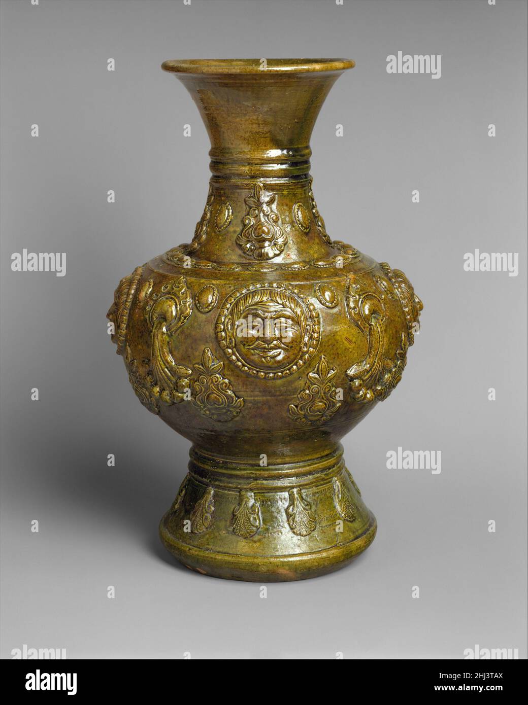 Vaso con facce umane metà 6th secolo Cina quattro rotonde di perle, ciascuna contenente la stessa immagine di un uomo frontale con un volto dell'Asia centrale, dominano questo vaso. Le teste frontali circondate da perle si presentano in diversi tipi di arte dell'Asia Centrale; per esempio, appaiono frequentemente su terracotta khotanese non smaltata.elementi della grammatica decorativa buddista appaiono qui pure: Le arlobi allungati sono caratteristiche delle immagini del Buddha, e le palme altamente stilizzate ricordano le incisioni in alcuni templi rupestri buddisti. I razionatori tasseled che emettono da un orname Foto Stock