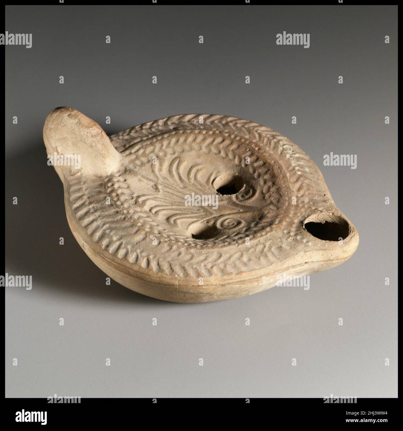 Lampada ad olio di terracotta 3rd sec. d.C. o successiva Loeschcke Roman tipo 8. Impugnatura non forata. Realizzato in stampo. Disco: Grande fronte palmo con diamante centrale sul gambo e due tendini a spirale alla base; due fori di riempimento verso i lati. Sulla spalla: Doppia corona d'aringa. Base concava profonda e indefinita, con lettere greche incise intorno al bordo sul retro: EΘƧXMS. Intatto... Lampada ad olio di terracotta 241591 Foto Stock