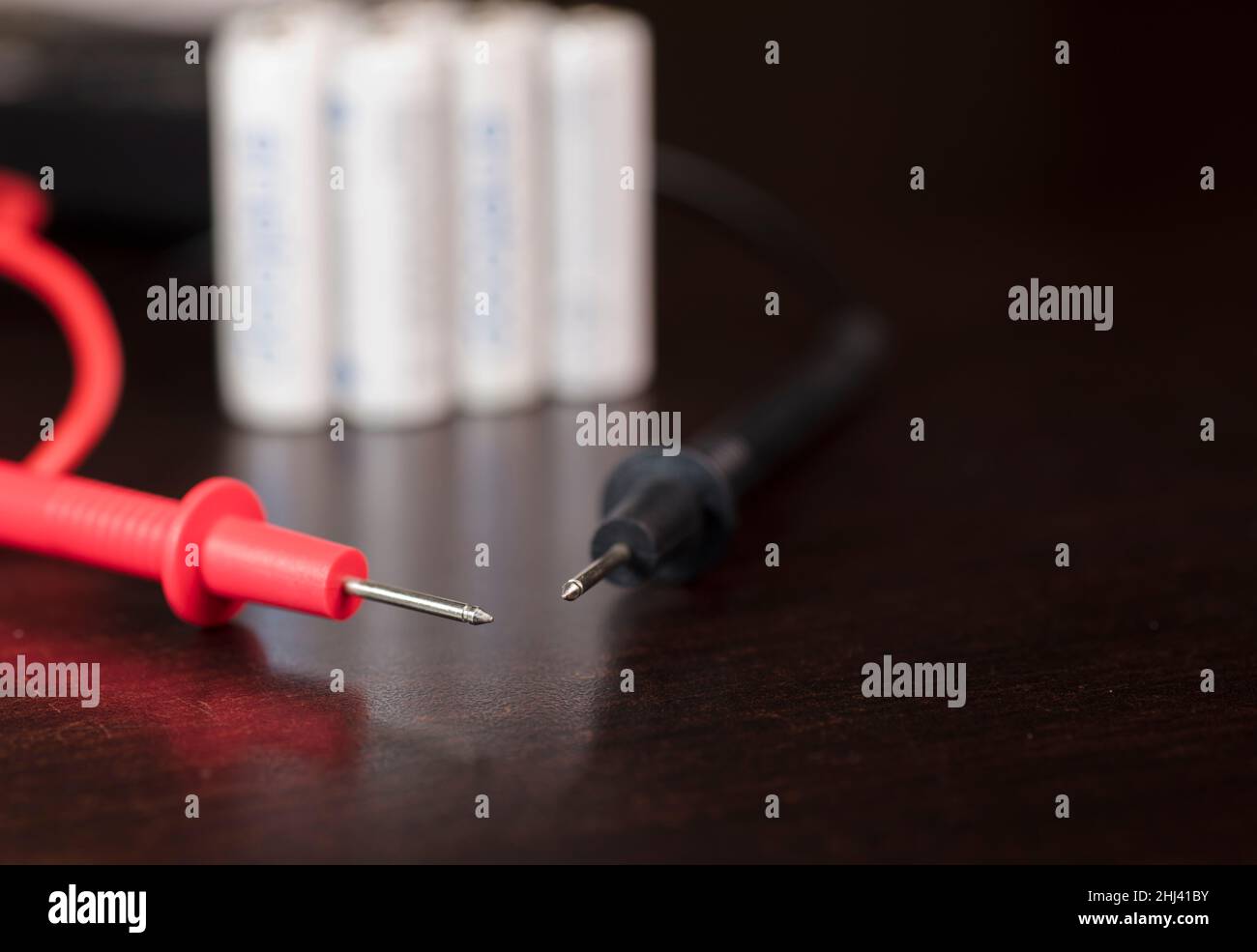 multimetro voltmetro, polo positivo rosso, polo negativo nero, batterie, su piano di lavoro giallo Foto Stock