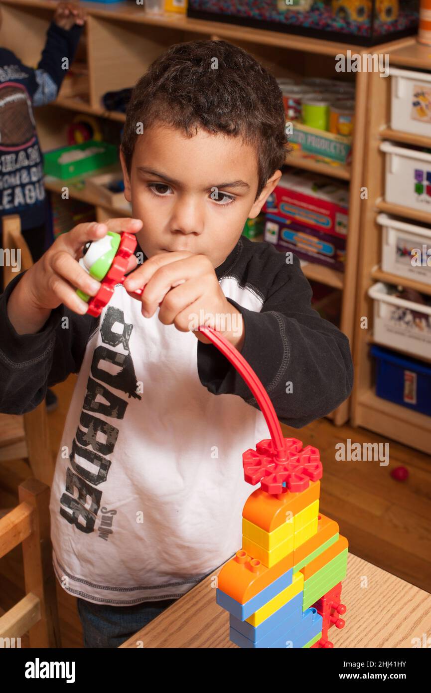 Istruzione ragazzo prescolare giocando con giocattolo da costruzione focalizzato sul mettere insieme i pezzi Foto Stock