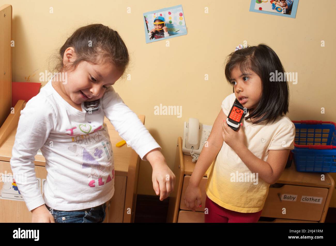 Istruzione Preschool 4-5 anni due ragazze fingono di giocare avendo simutaneous le converstations del telefono levandosi in piedi fianco a fianco nella zona della famiglia della cucina Foto Stock