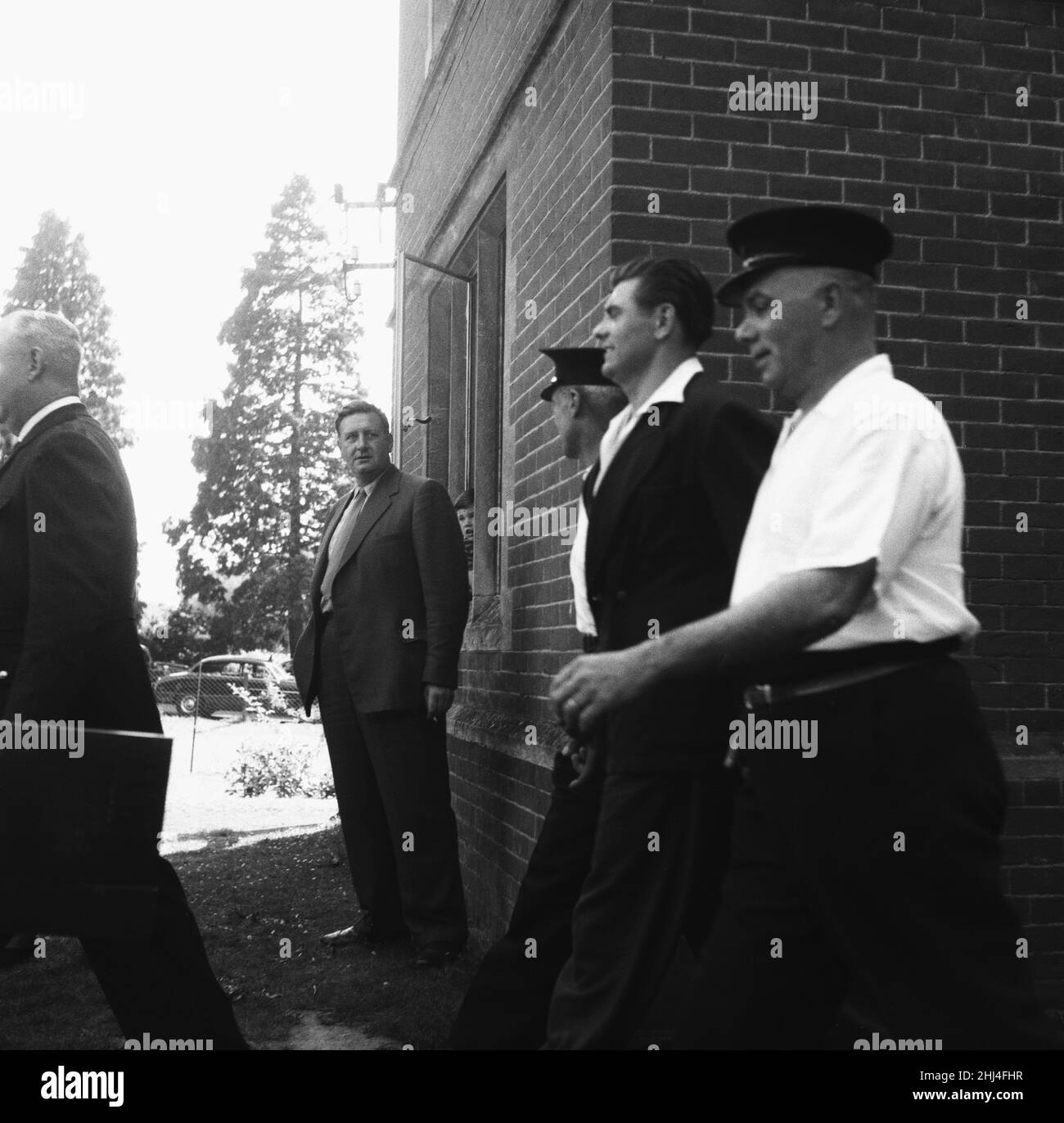 Frank Mitchell, il Mad Axman, fuggito dalla prigione di Broadmoor, è condotto lontano dalla stazione di polizia di Hartley Wintney dopo essere stato riconquistato su un allenatore di Bournemouth in Hampshire diretto a Londra. In seguito, fuggì dalla prigione di Dartmoor nel 1966 con l'aiuto di Reggie e Ronnie Kray. 9th luglio 1958. Foto Stock