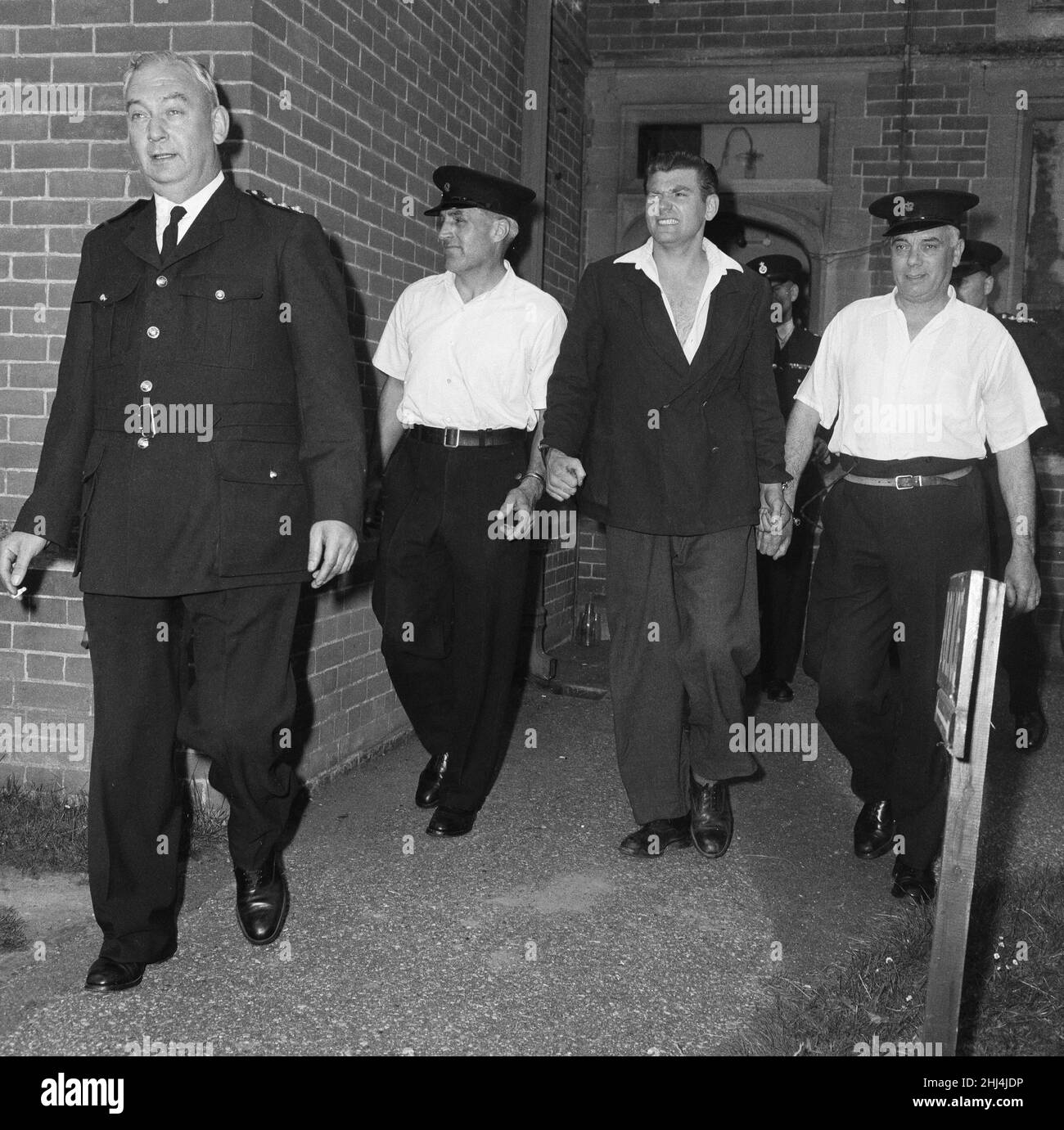 Frank Mitchell, il Mad Axman, fuggito dalla prigione di Broadmoor, è condotto lontano dalla stazione di polizia di Hartley Wintney dopo essere stato riconquistato su un allenatore di Bournemouth in Hampshire diretto a Londra. In seguito, fuggì dalla prigione di Dartmoor nel 1966 con l'aiuto di Reggie e Ronnie Kray. 9th luglio 1958. Foto Stock