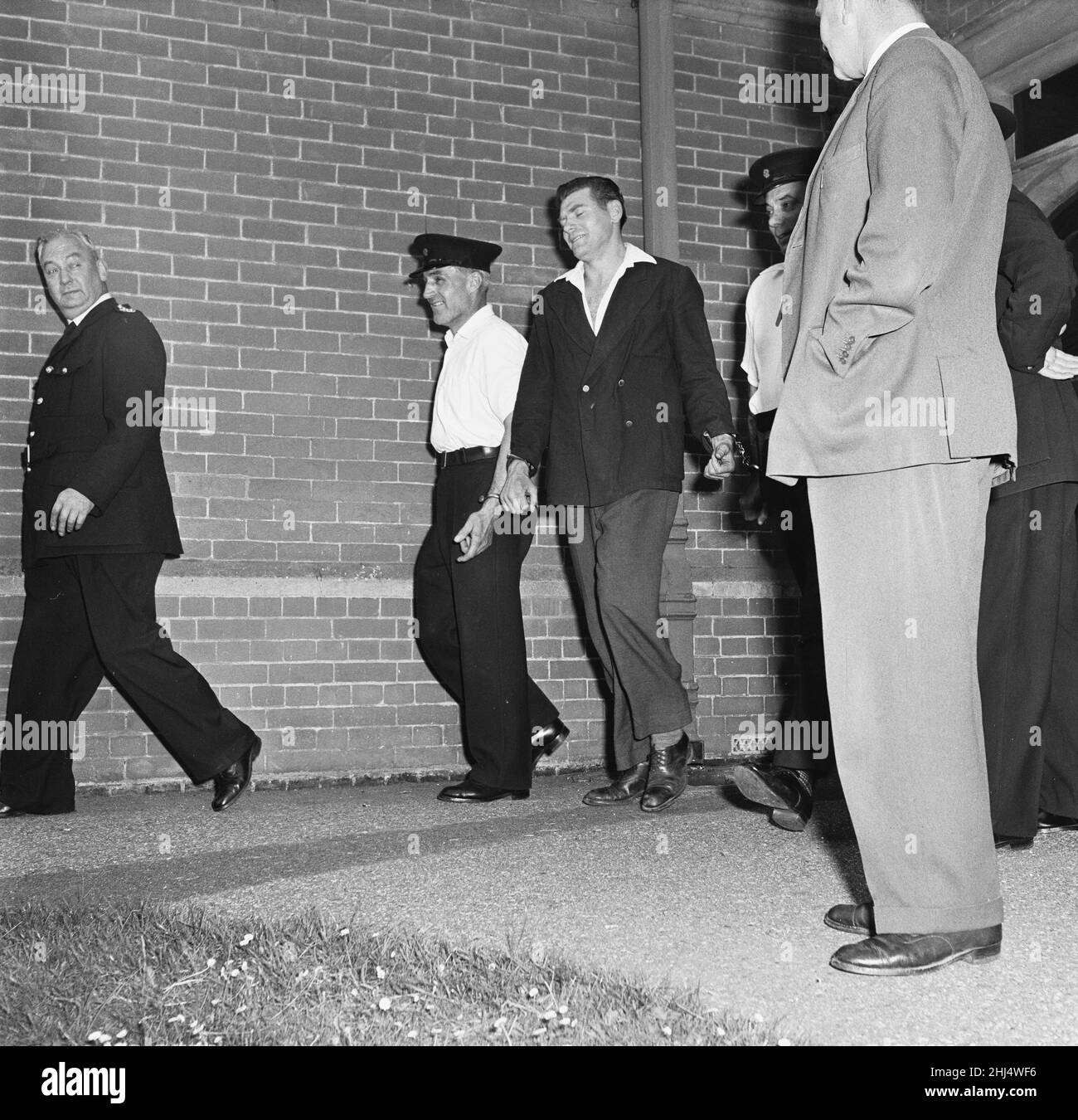 Frank Mitchell, il Mad Axman, fuggito dalla prigione di Broadmoor, è condotto lontano dalla stazione di polizia di Hartley Wintney dopo essere stato riconquistato su un allenatore di Bournemouth in Hampshire diretto a Londra. In seguito, fuggì dalla prigione di Dartmoor nel 1966 con l'aiuto di Reggie e Ronnie Kray. 9th luglio 1958. Foto Stock