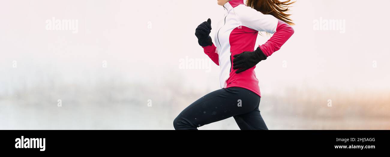 Inverno fitness donna che corre in abiti freddi indossando guanti e pantaloni termali, giacca jogging in bianco neve sfondo panorama Foto Stock