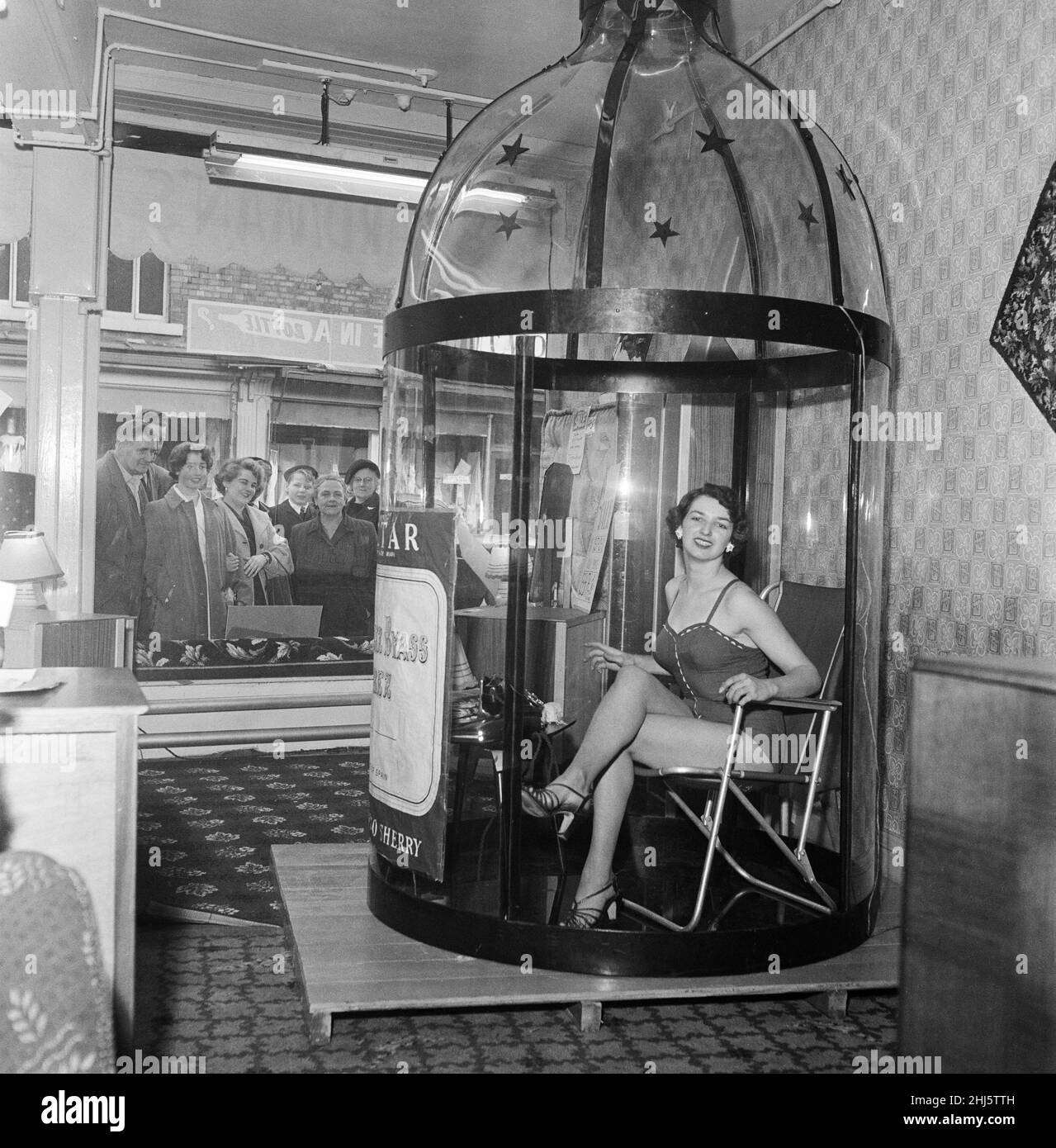 Angela Martin (22 anni) si inginocchiò e legge mentre si siede in una bottiglia, nella vetrina di un negozio di mobili a Rochdale, Greater Manchester. 23rd ottobre 1957. Foto Stock