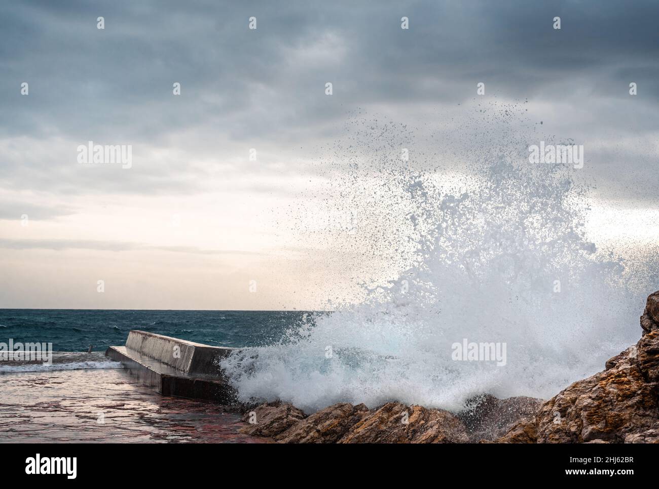 Grande onda spruzzi sul molo. Grande onda di mare in una giornata ventosa. Le onde si infrangono contro il frangiflutti di cemento all'ingresso del porto. Onde giganti che si infrangono sul frangiflutti Foto Stock