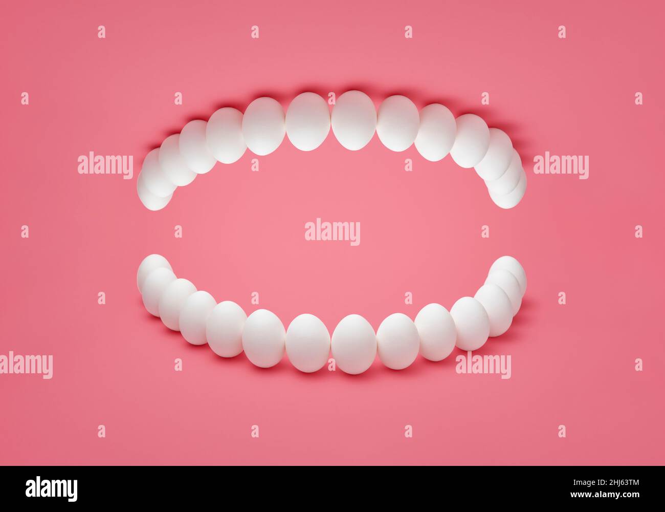 Concept fotografico con uova di pollo disposte su sfondo rosa come la dentiera umana. Replica dei denti umani a base di uova di pollo. Foto Stock