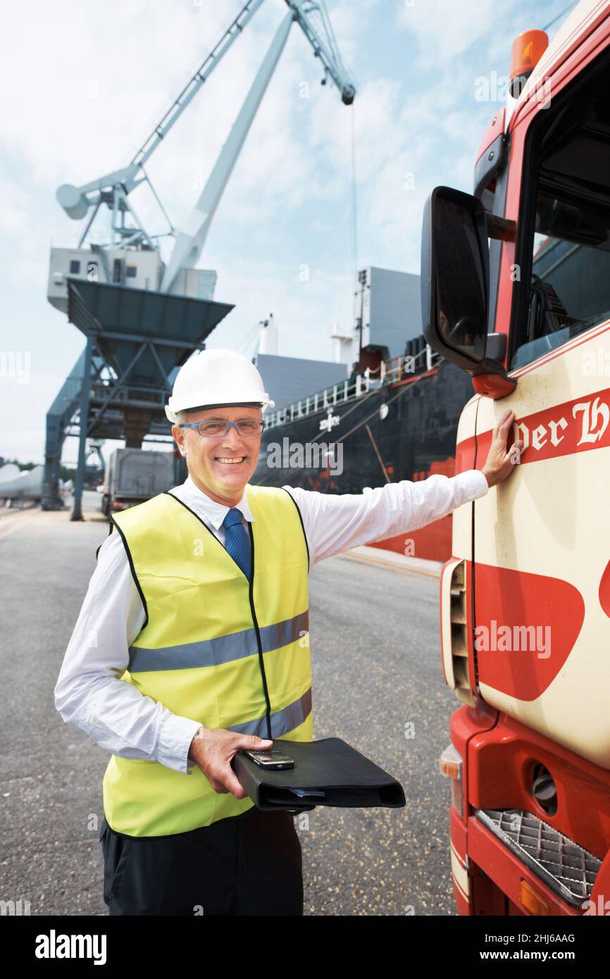 Il trasporto garantisce il successo del commercio. Ritratto di un lavoratore portuale in piedi al porto in mezzo all'attività dell'industria marittima. Foto Stock