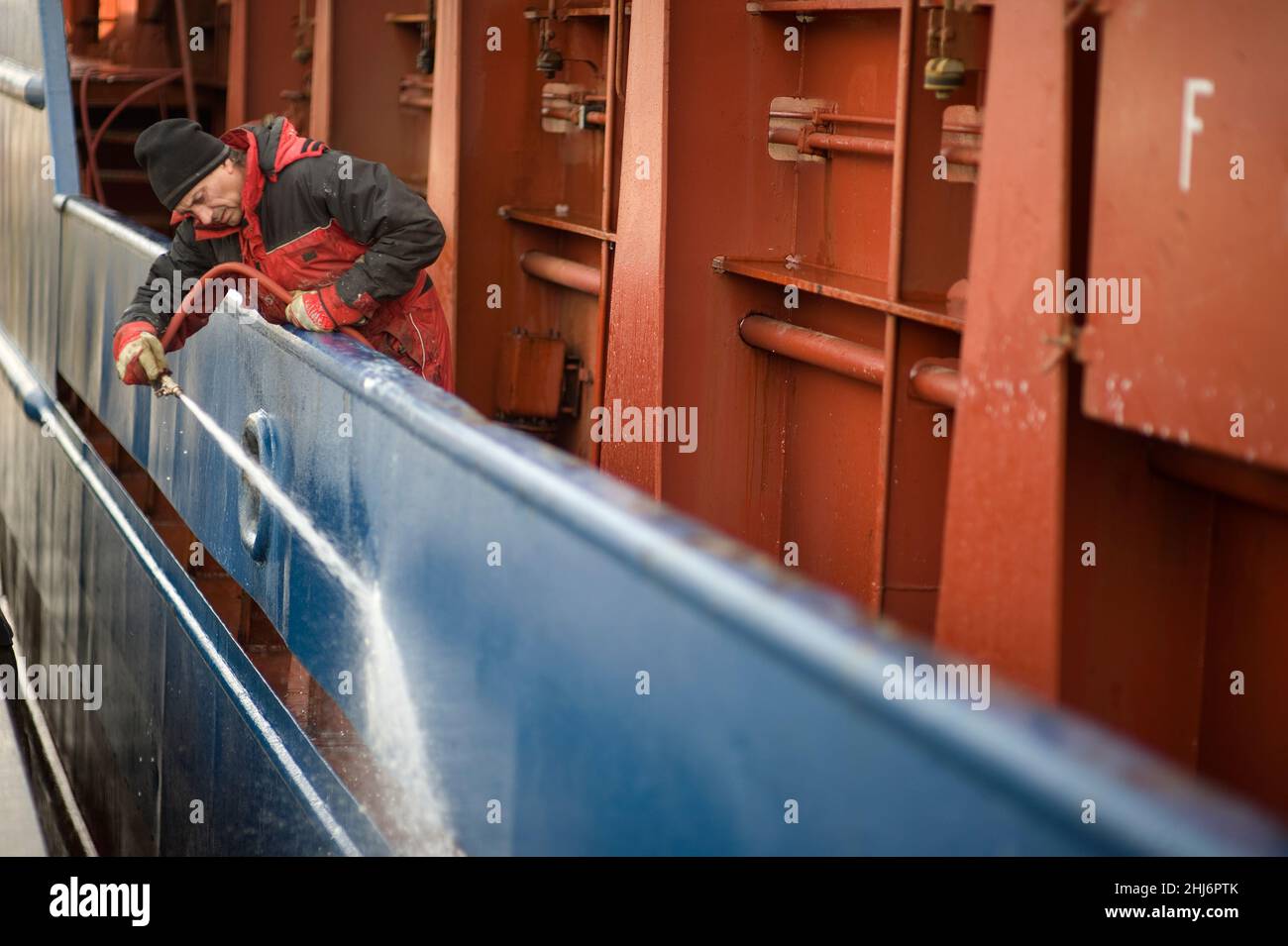 Rotterdam, Paesi Bassi. Russo, in grado Seaman pulizia la Holl del mare andando nave lavora su usando un tubo spruzzando acqua. Foto Stock