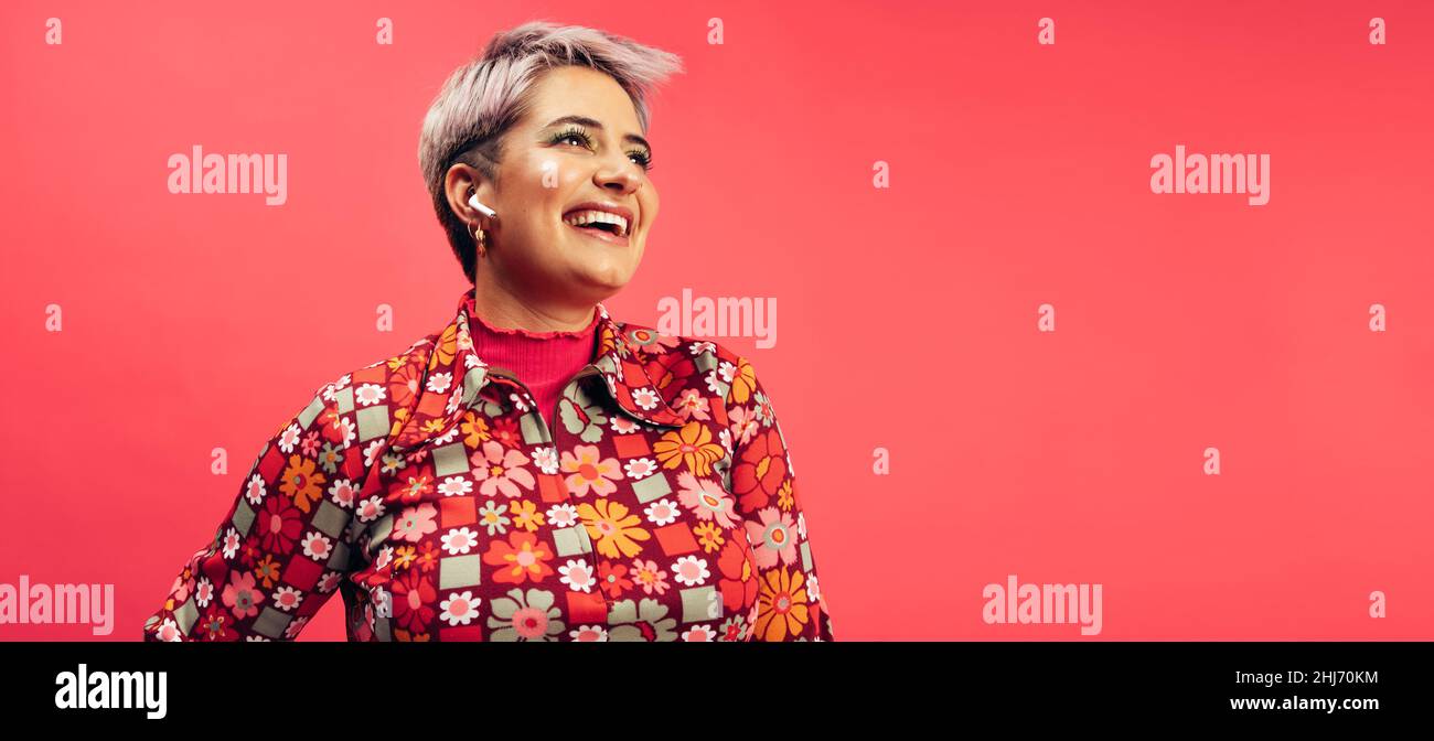 Streaming di un podcast di ispirazione. Spensierate la giovane donna sorridendo allegro mentre indossate gli auricolari senza fili. Giovane donna con capelli tinti che la ascoltano Foto Stock
