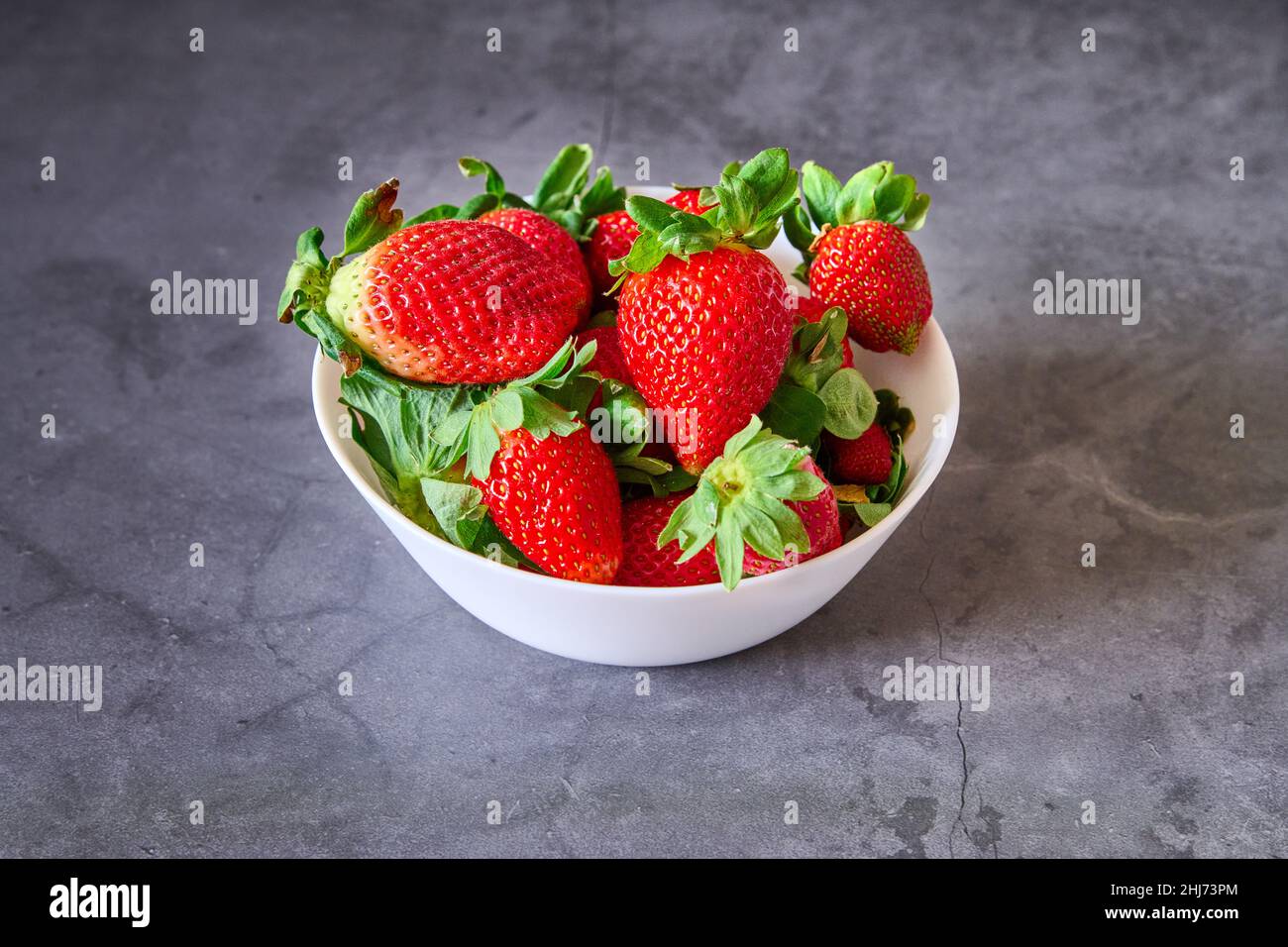 Una ciotola bianca con fragole su sfondo nero di ardesia Foto Stock