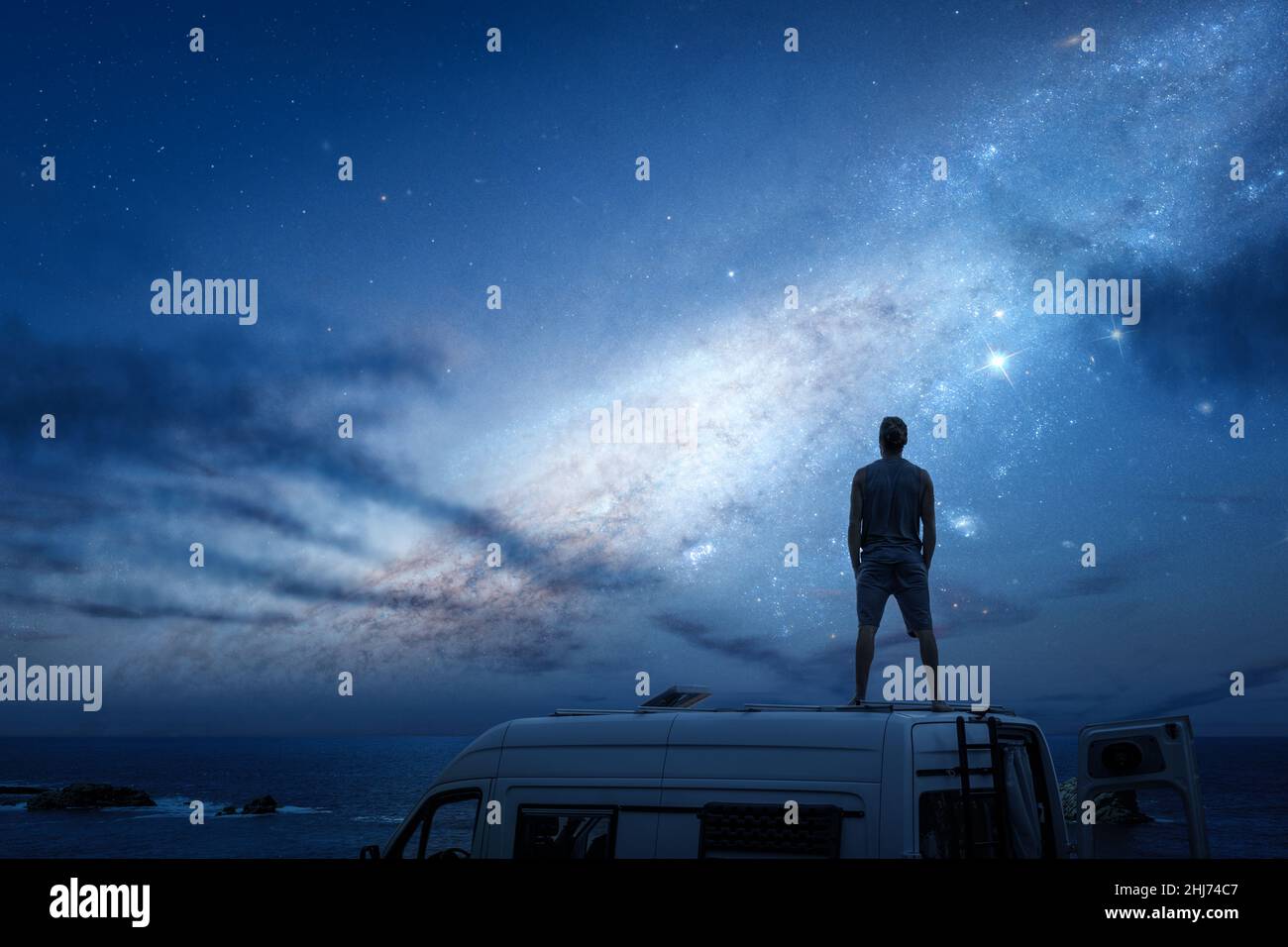 Cielo stellato sopra un uomo in piedi sul tetto del suo camper Foto Stock