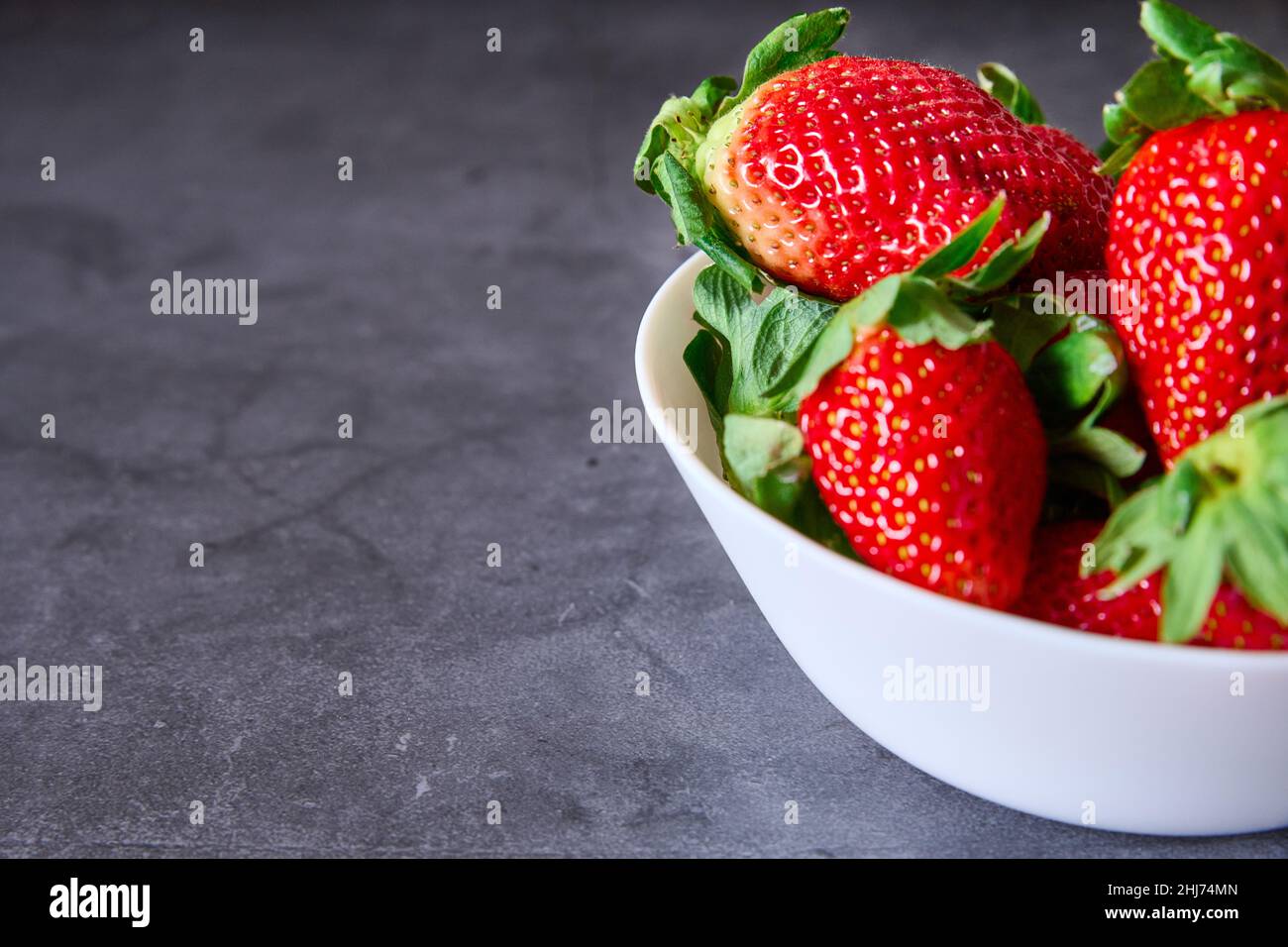 Una ciotola bianca con fragole su sfondo nero di ardesia Foto Stock