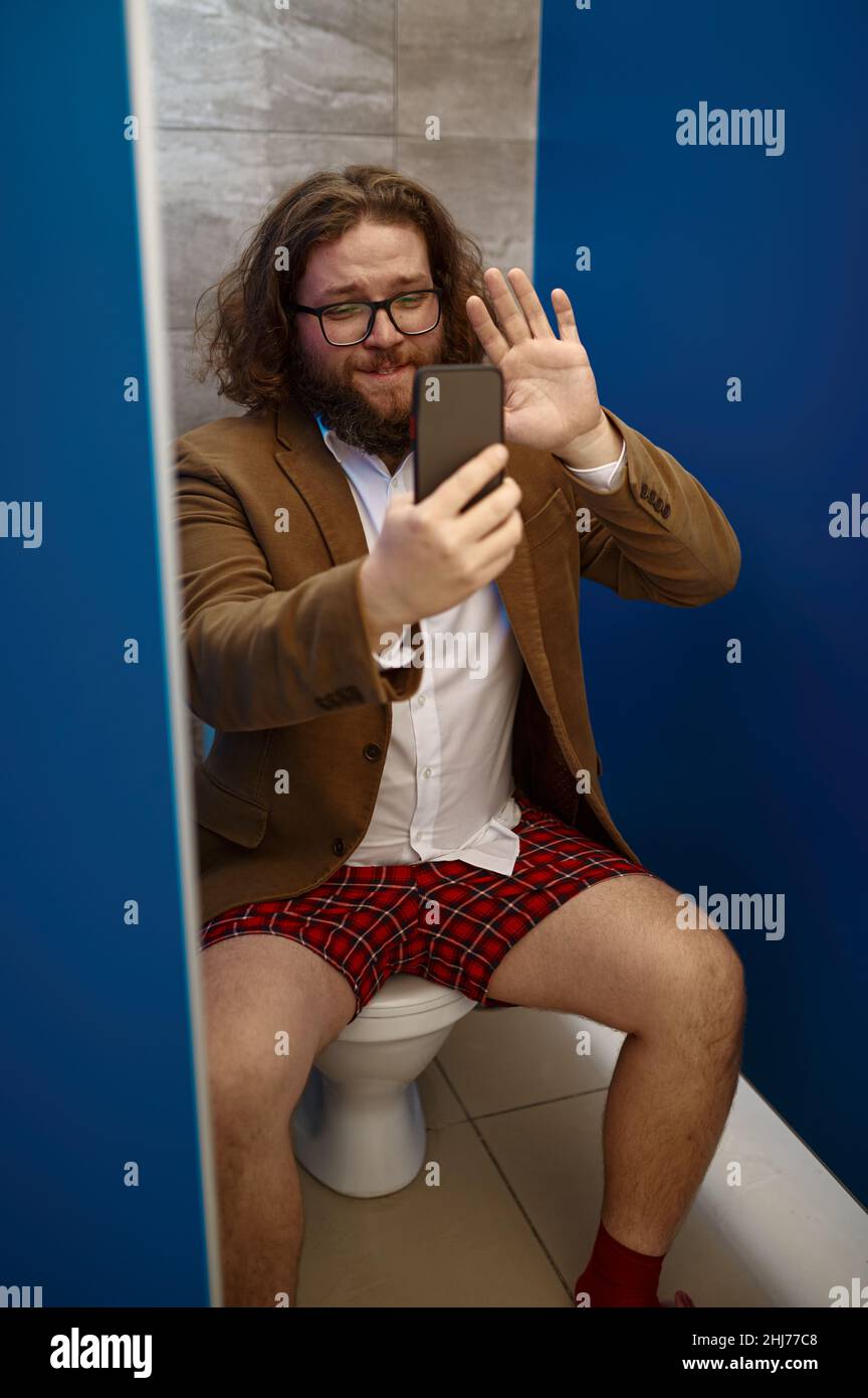 Uomo d'affari che parla al telefono mentre si siede sul gabinetto Foto Stock