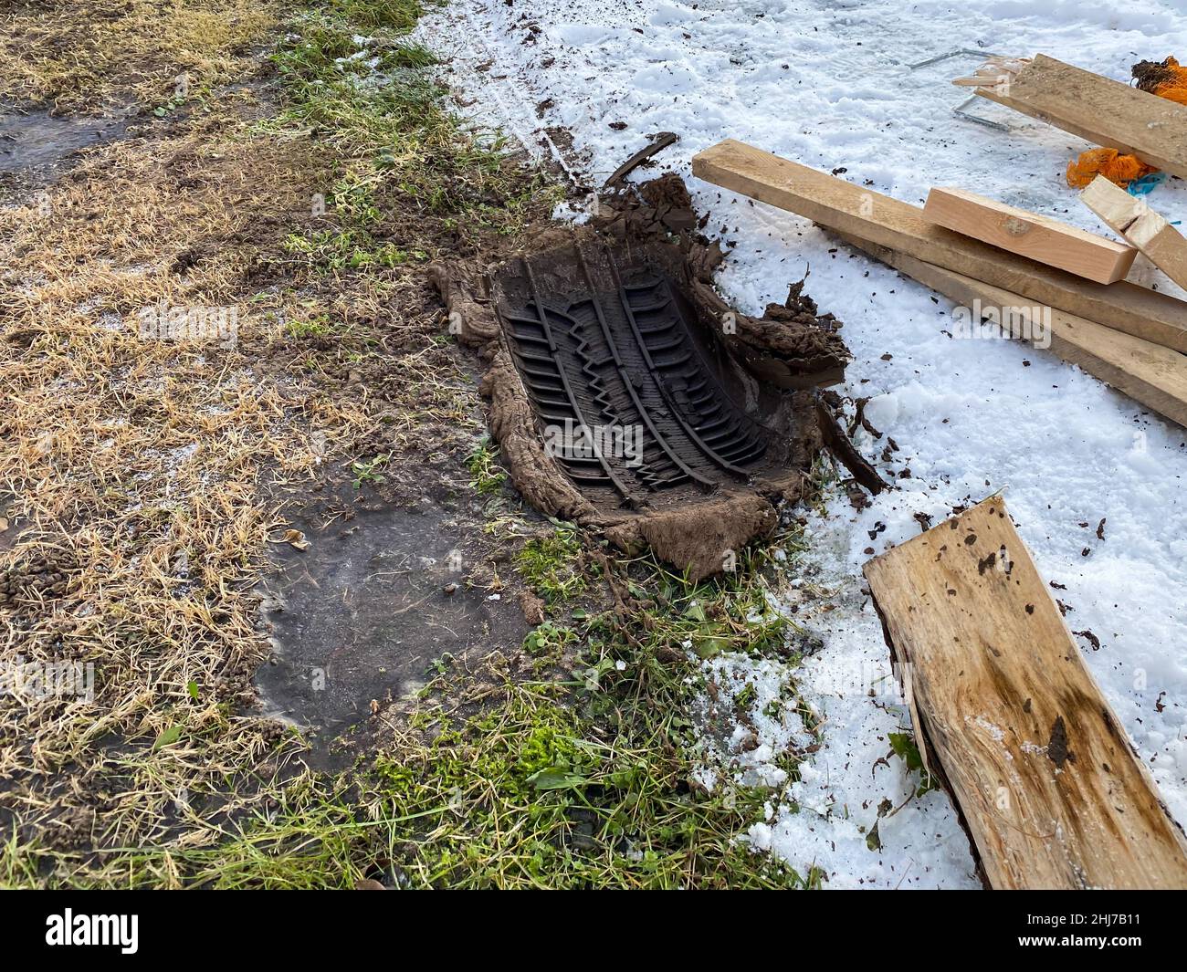 Pneumatici auto battistrada piedi in primavera. Ingombro pneumatico bloccato per auto, con tavole di legno accanto ad esso. Prato. Script. Sfondo marrone astratto. Piede della ruota dell'auto Foto Stock