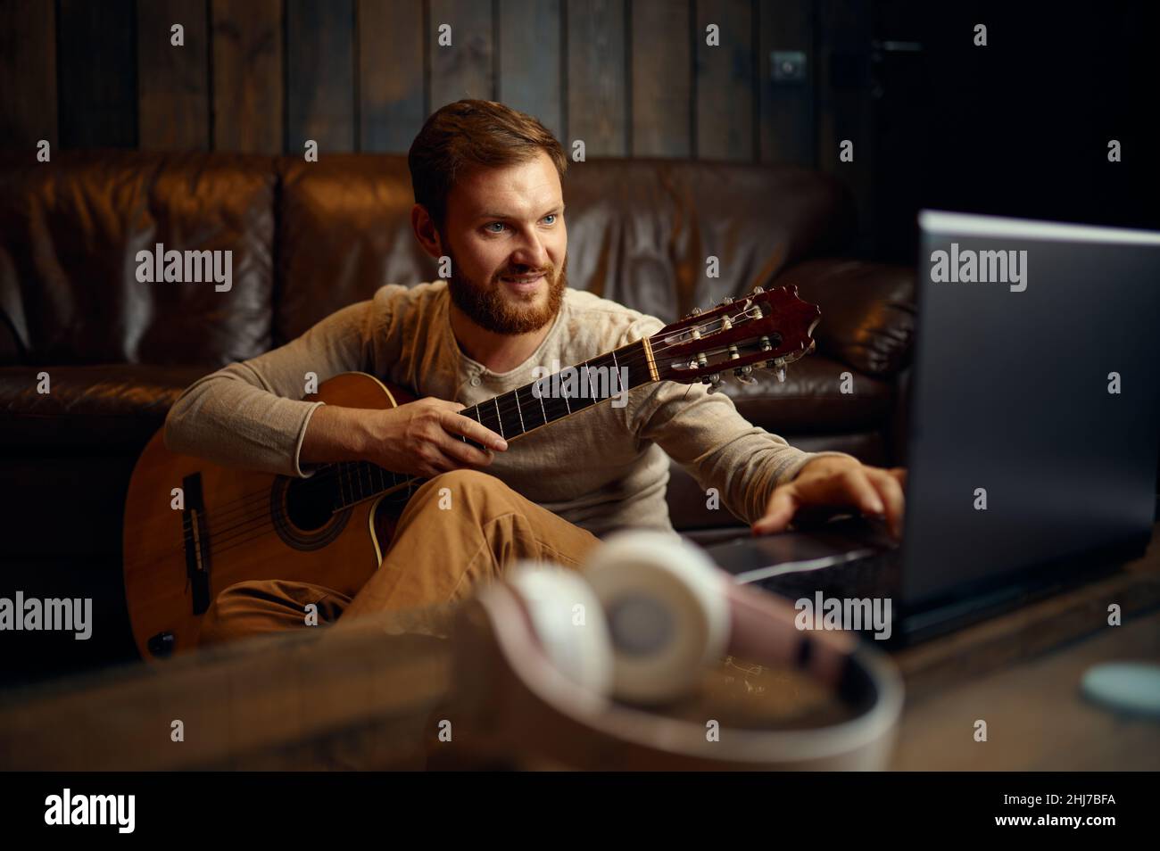 Uomo che suona la chitarra mentre guarda il laptop Foto Stock