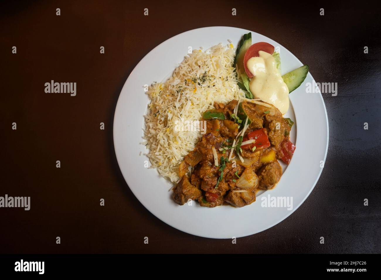 Carne e verdure cotte in una salsa piccante, curry indiano con riso e decorazione insalata su un piatto bianco e un tavolo di legno marrone, spazio copia, alto A. Foto Stock