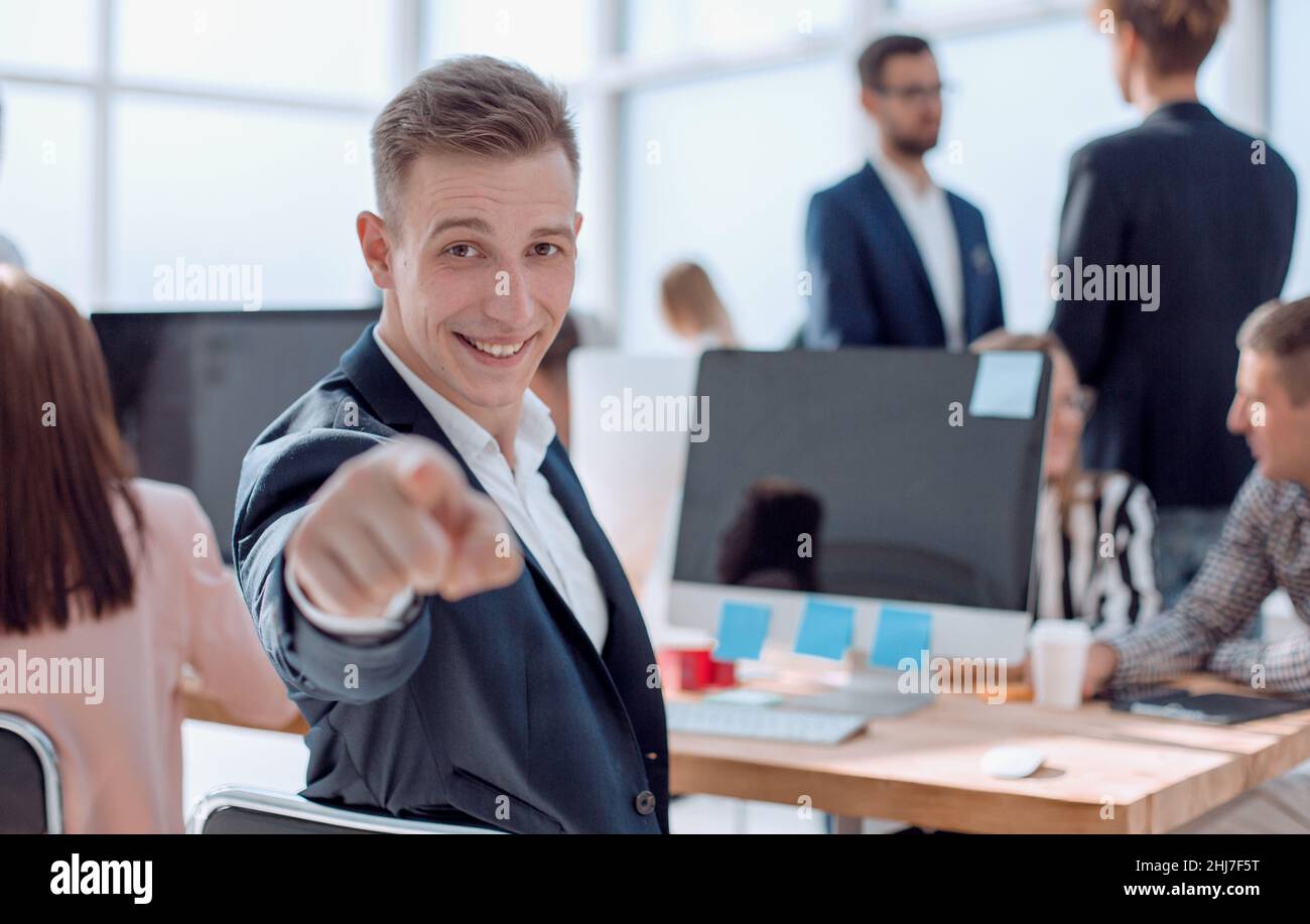 Sorridente giovane impiegato seduto alla sua scrivania e indicando voi Foto Stock