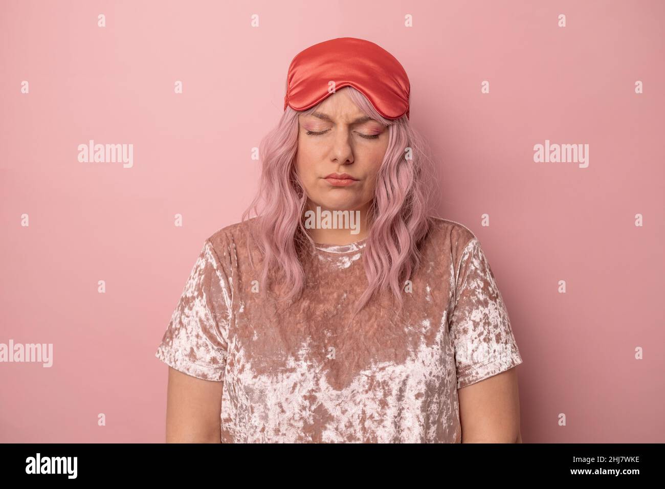 La donna addormentata con occhi chiusi indossa la maschera del sonno, triste svegliarsi presto al mattino isolato su sfondo rosa. Foto Stock