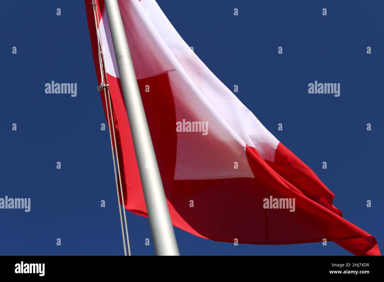 La bandiera della Svizzera durante una giornata ventosa. Primo piano della bandiera rossa e bianca con cielo blu sullo sfondo. Simbolo di indipendenza e nazionalità. Foto Stock