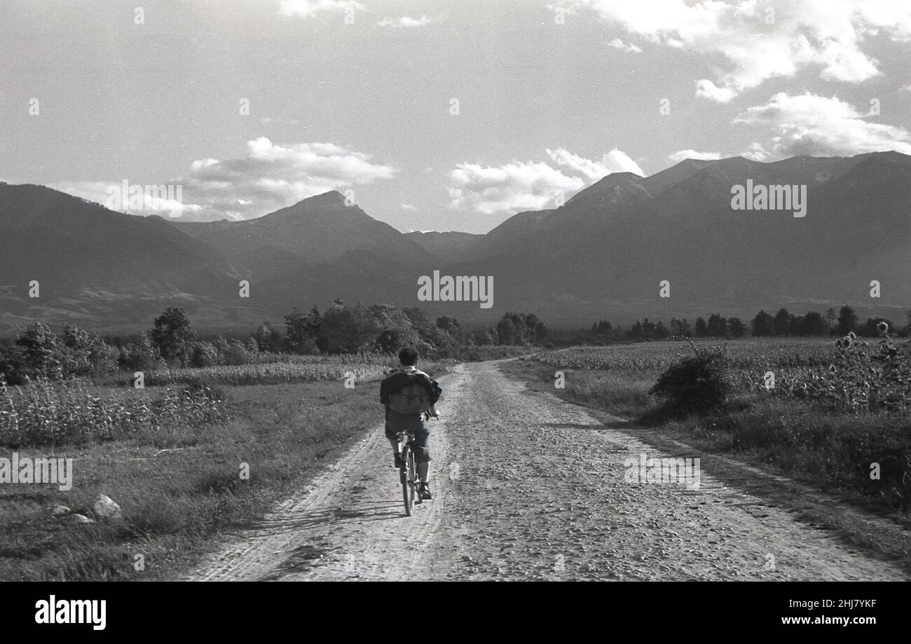 1933, storico, fuori su una pista di ghiaia, un uomo slavo locale sulla sua bicicletta, portando merci sul suo corpo superiore, Jugoslavia, Alpi Dinariche in lontananza. Foto Stock
