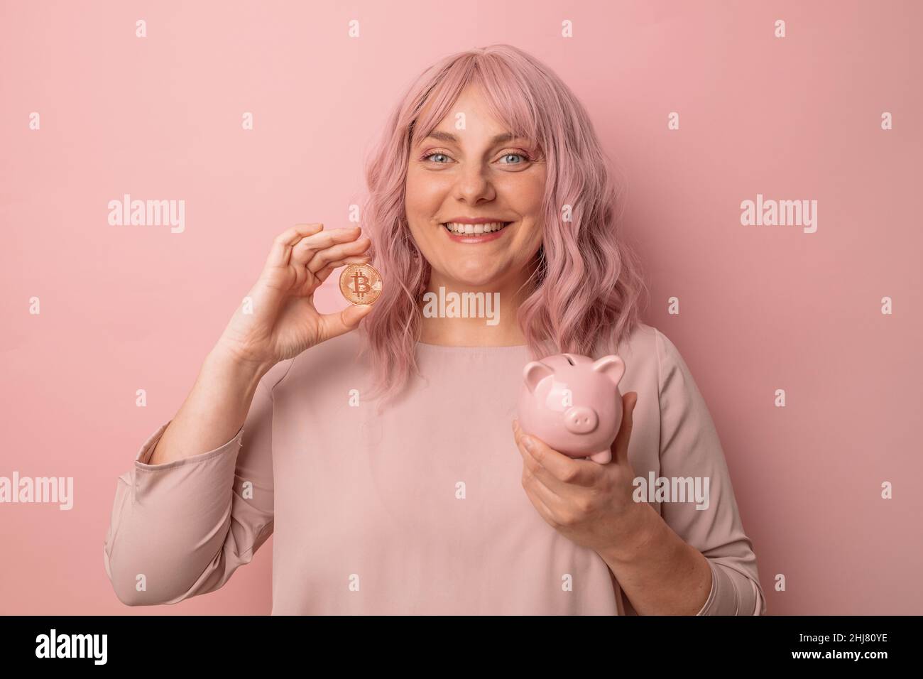 Positivo giovane bella donna attraente business sorridente tenendo un piggybank per investimenti su sfondo rosa chiaro, copyspace Foto Stock