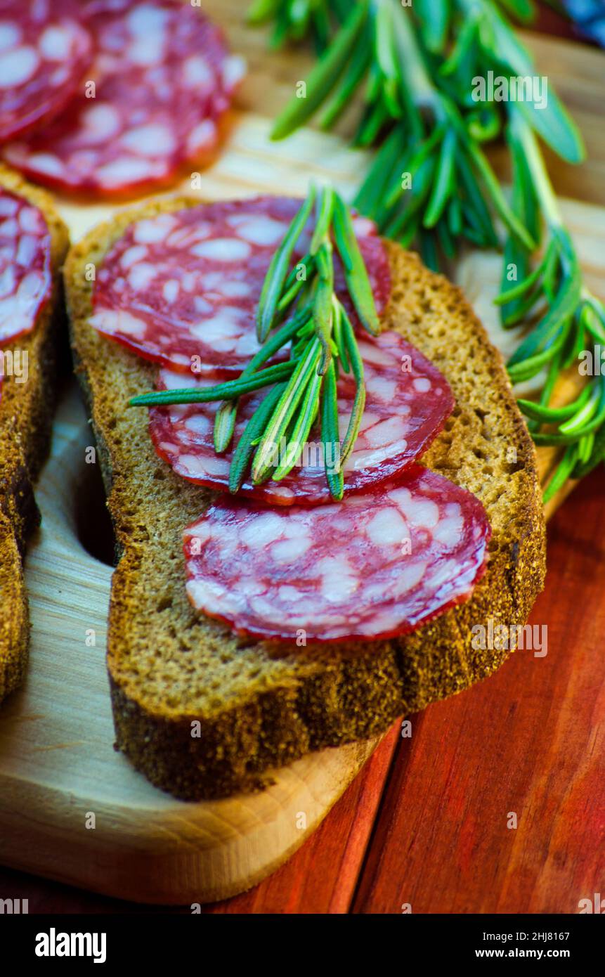 sandwich con salsiccia su un asse di legno e spezie primo piano Foto Stock