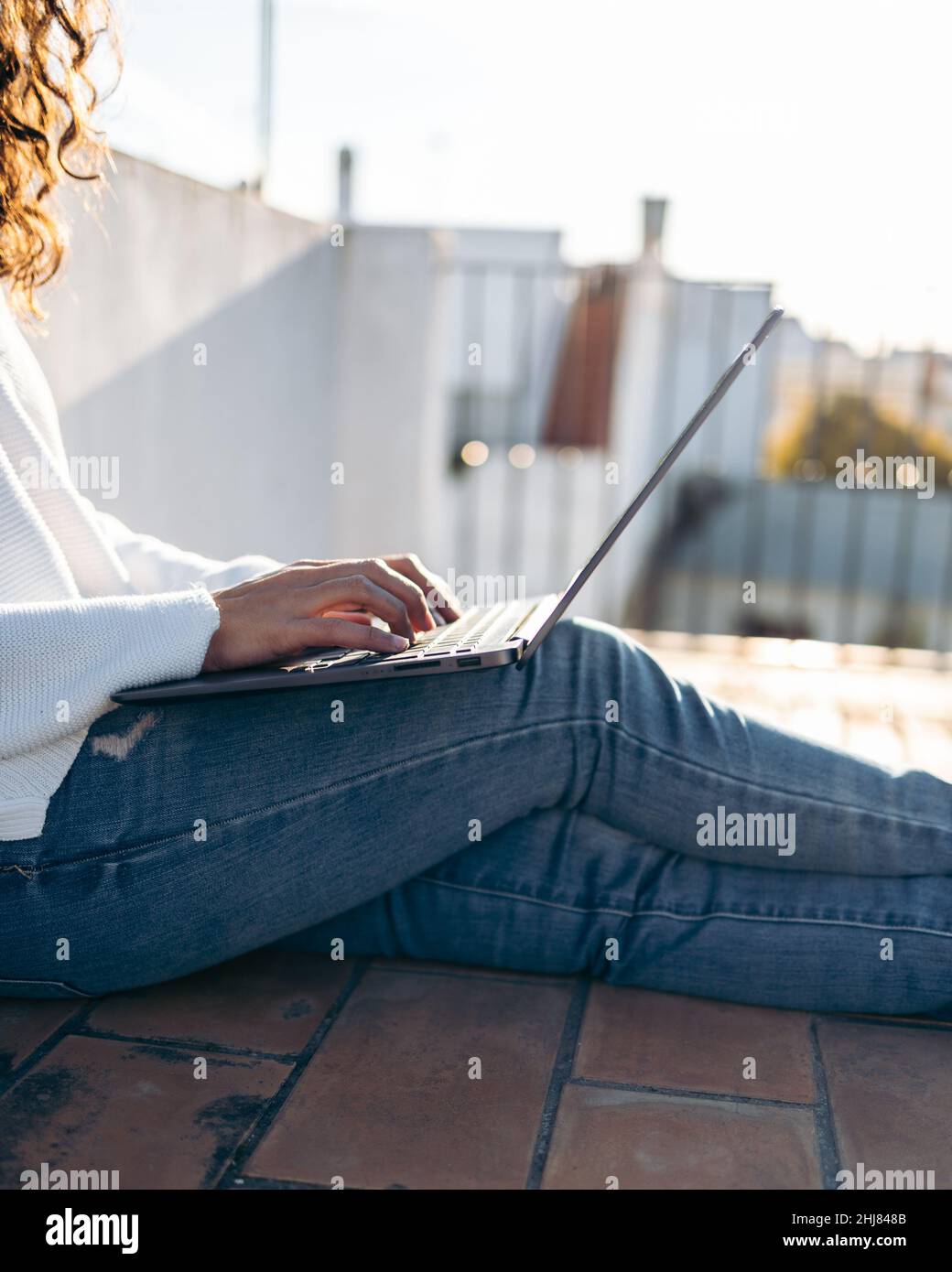 Primo piano di una donna irriconoscibile che lavora con il suo computer portatile seduto sul pavimento in terrazza Foto Stock