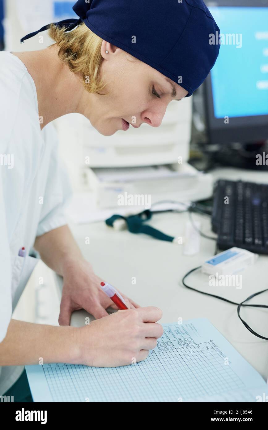 Il lato amministrativo della doctoring. Shot di un giovane chirurgo che riempie la documentazione in un ospedale. Foto Stock