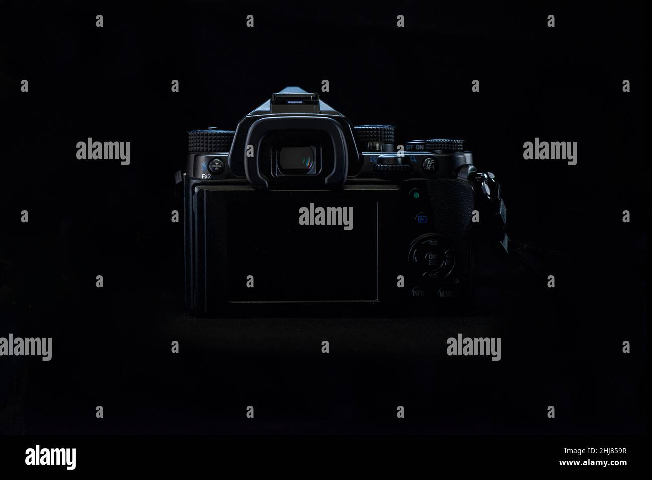 Luce a tasti bassa, lato posteriore di una DSLR con corpo nero su sfondo nero, che mostra lo schermo LCD spento, con una luce sul bordo del corpo della fotocamera. Foto Stock