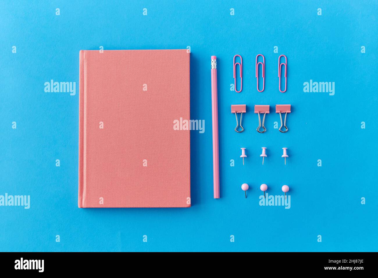notebook rosa, spille, clip e matita su blu Foto Stock