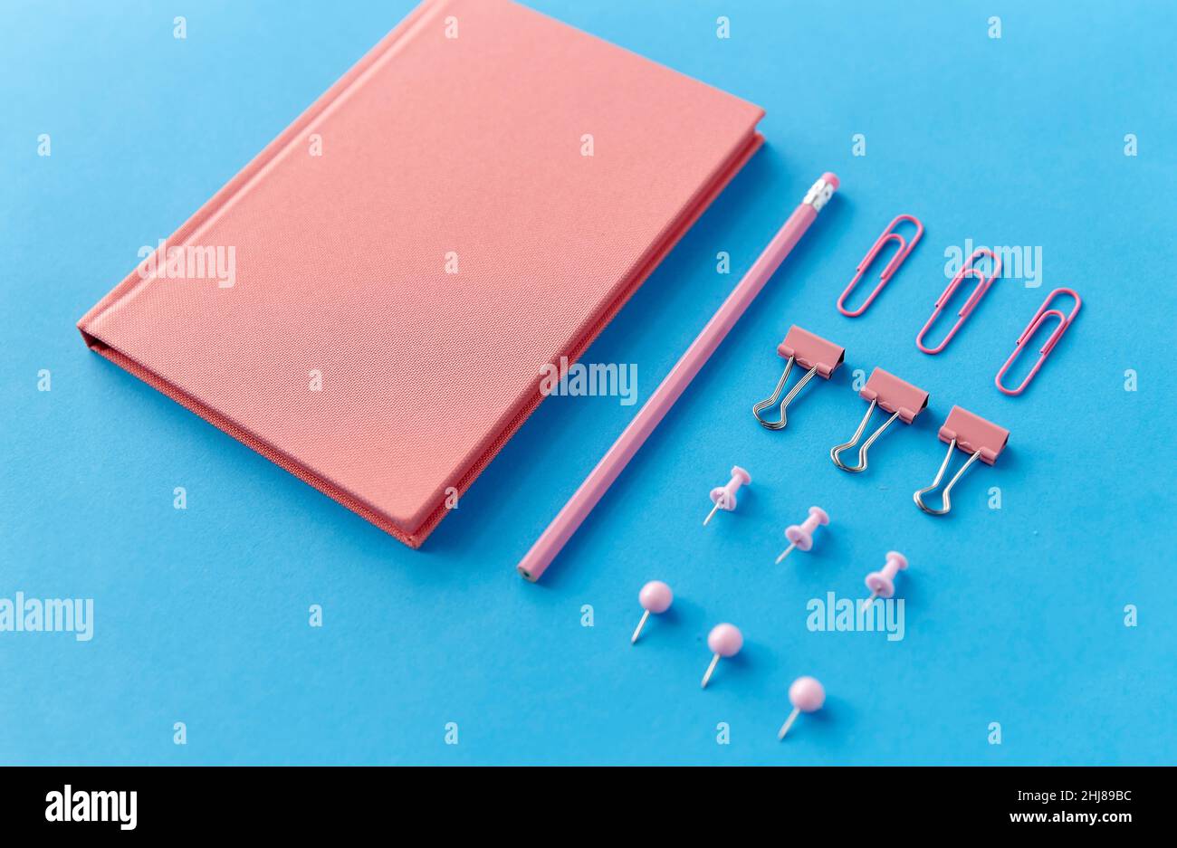 notebook rosa, spille, clip e matita su blu Foto Stock