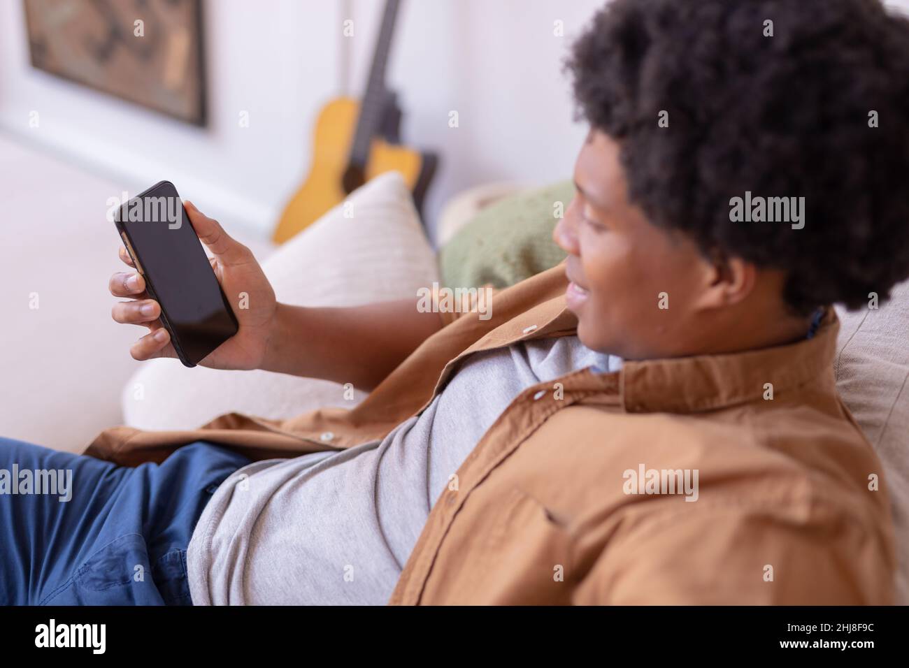 Sorridente giovane afroamericano che usa uno smartphone con spazio vuoto, spazio copia. Inalterato, stile di vita, attività per il tempo libero, tecnologia wireless, sociale Foto Stock