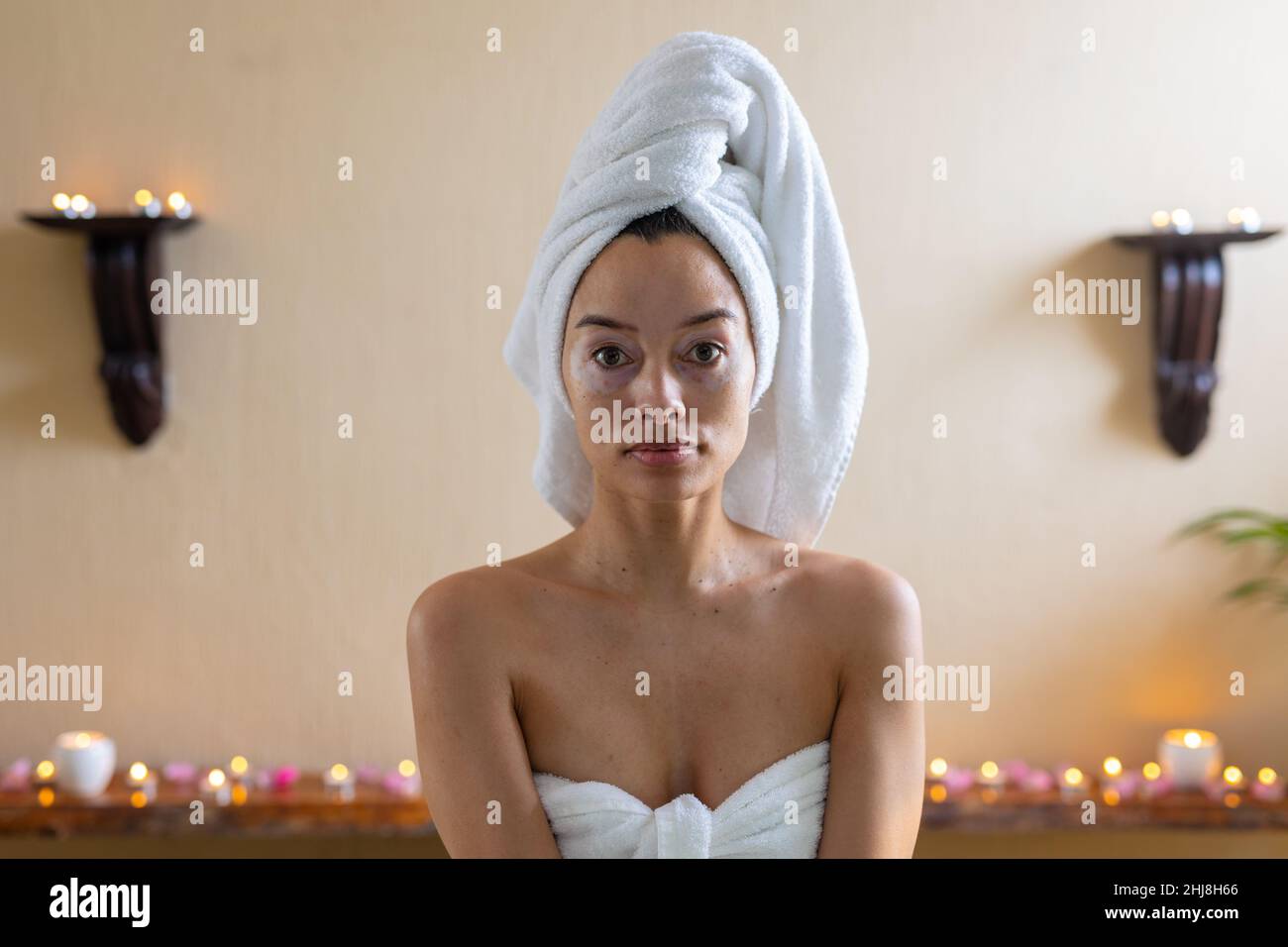 Ritratto di giovane donna biraciale con asciugamano avvolto sulla testa e sul corpo seduta in spa, spazio copia. spa, cura del corpo, stile di vita, vitiligo e benessere. Foto Stock