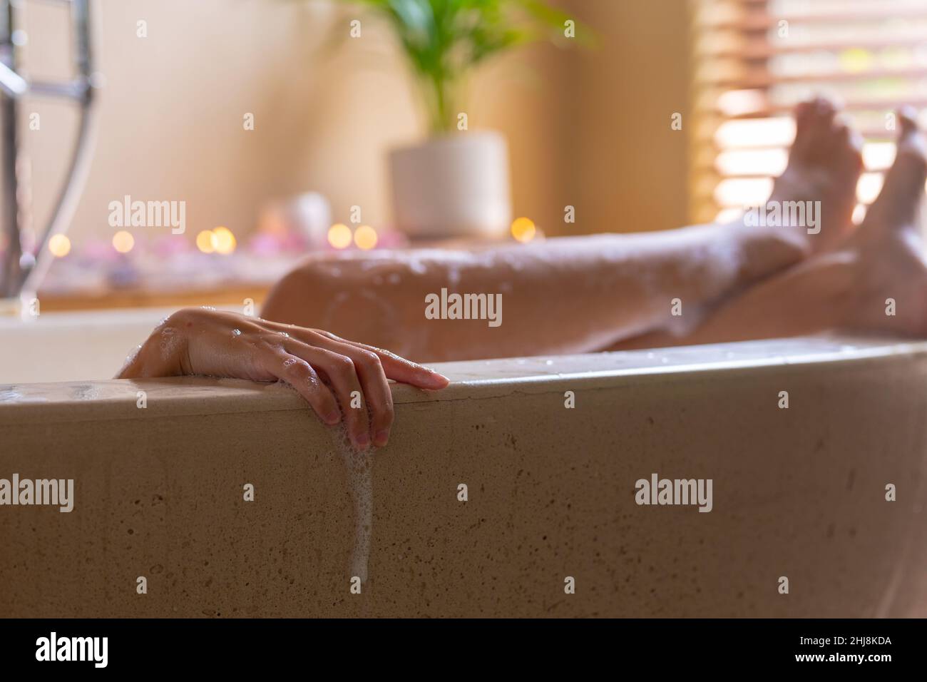Sezione bassa di giovane donna biraciale con gambe incrociate alla caviglia in vasca da bagno presso la spa. Inalterato, spa, cura del corpo, stile di vita e benessere. Foto Stock