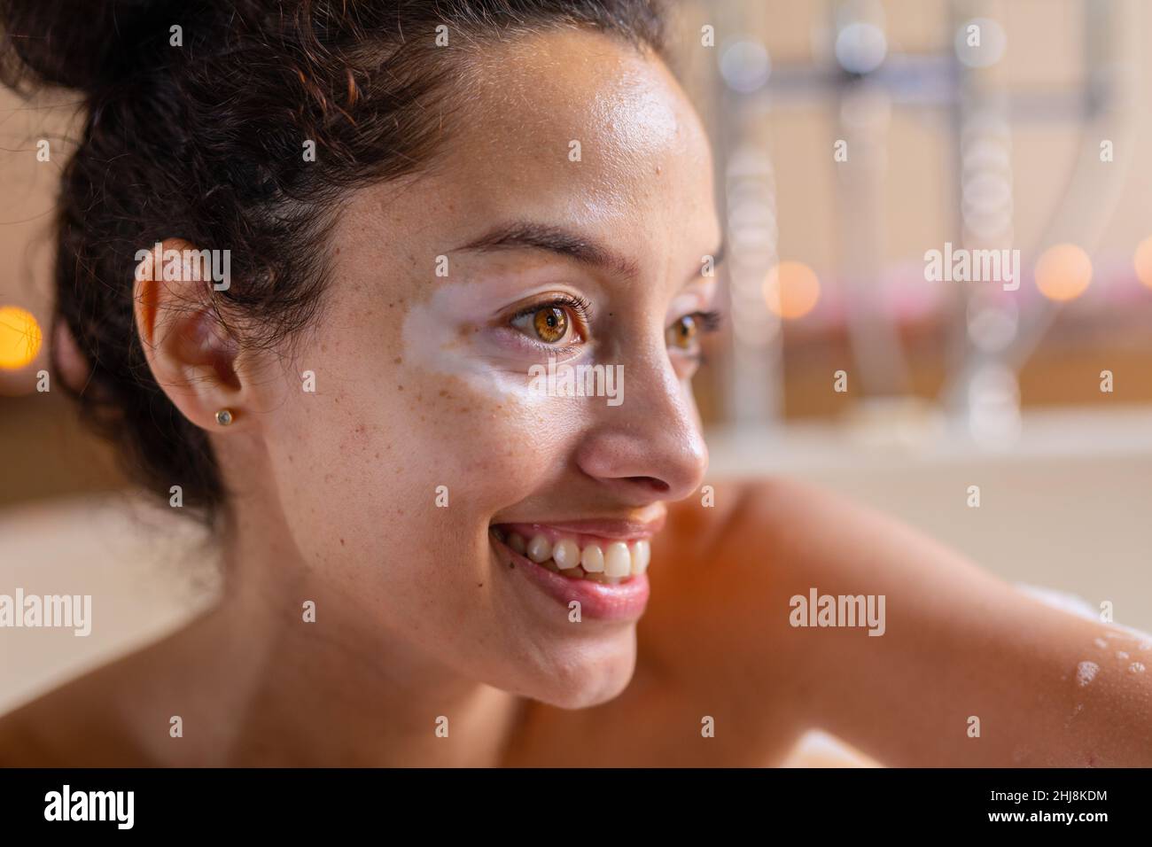 Primo piano di sorridente ragazza biraciale bella guardando via nella vasca da bagno al centro benessere. Inalterato, spa, cura del corpo, stile di vita, vitiligo e benessere. Foto Stock