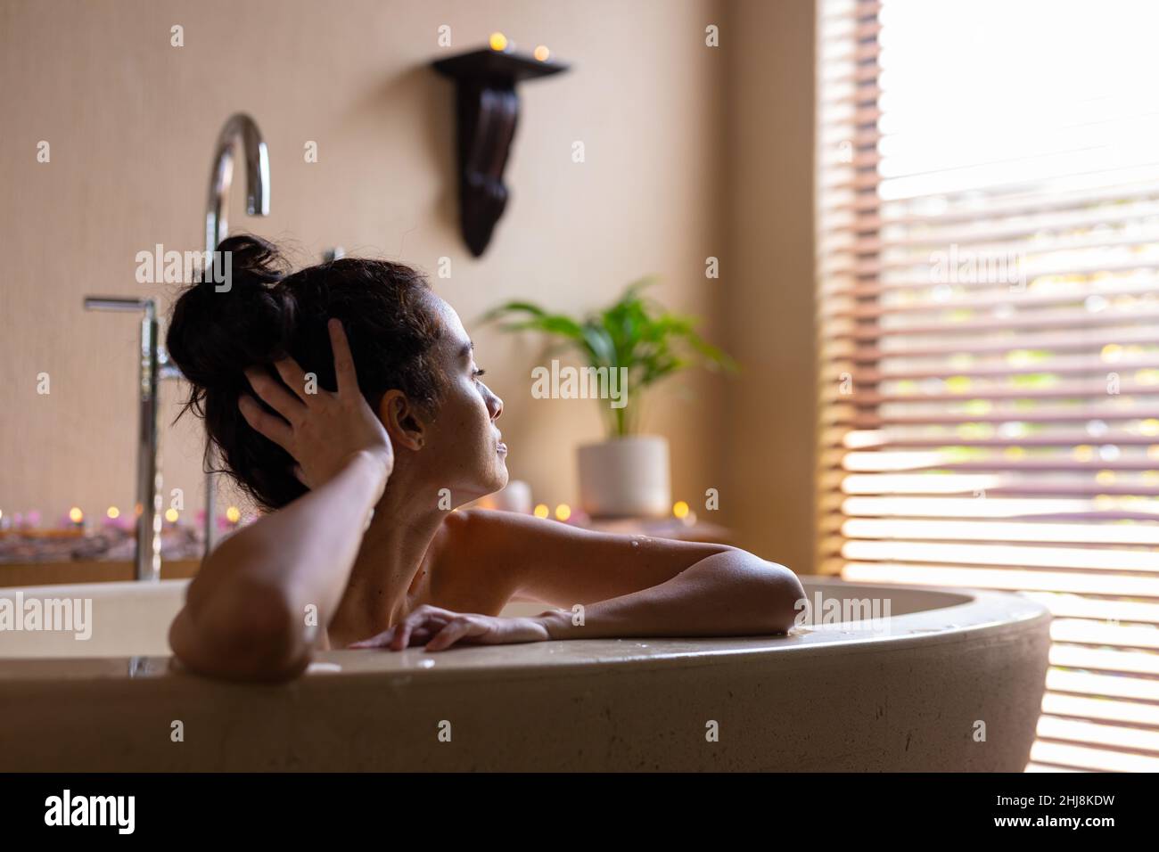 Giovane donna biraciale pensata sulla vasca da bagno della spa. Inalterata, spa, cura del corpo, stile di vita, solitudine, vitiligo e benessere. Foto Stock