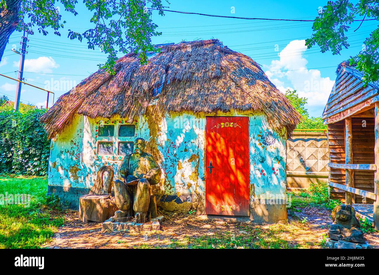 La piccola casa rurale Ucraina shabby con tetto di paglia e una scultura in legno di cossack in un parco di Zaporizhzhia, Ucraina Foto Stock